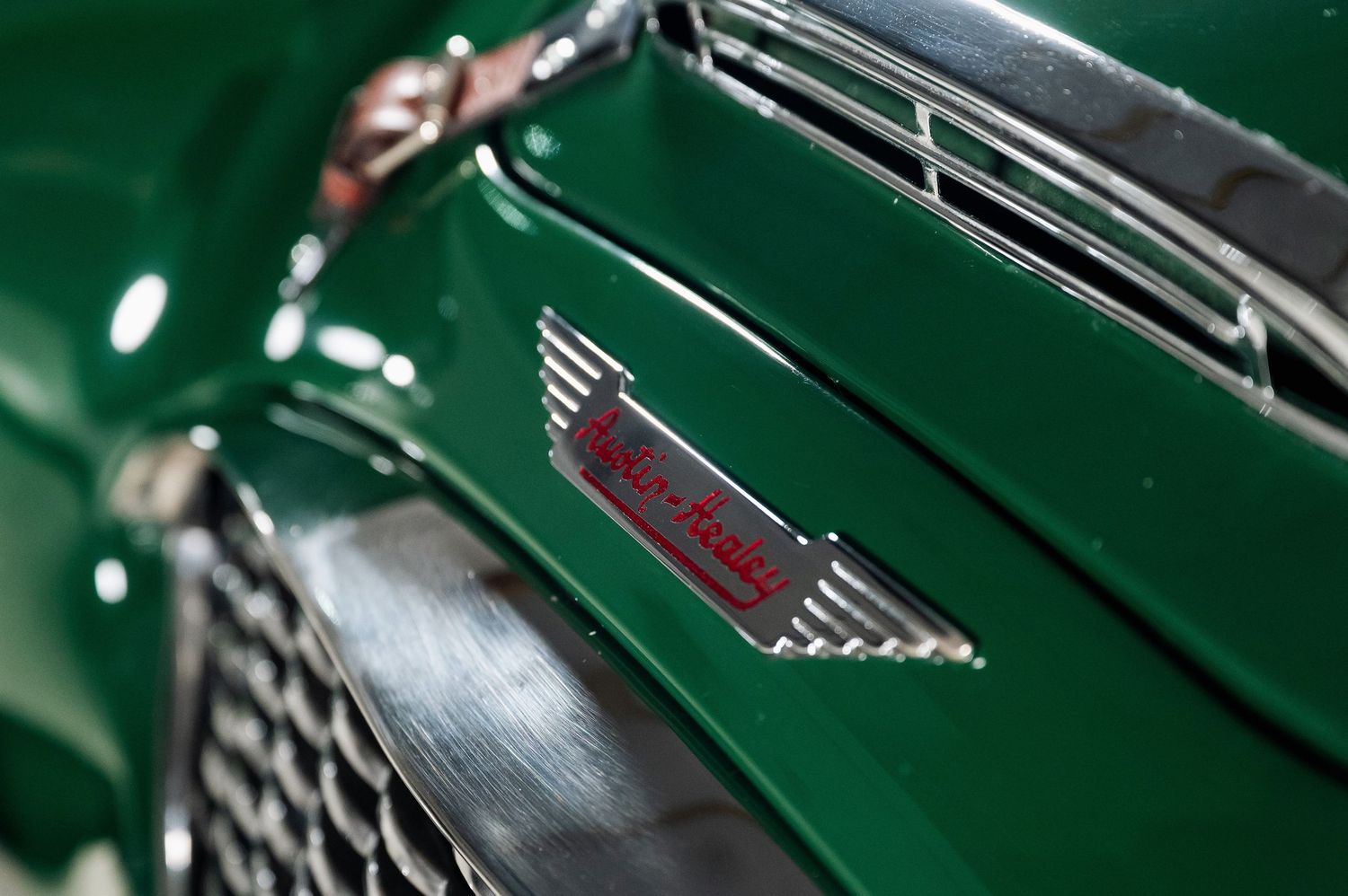 Close-up of a vintage green car badge reading Sport Road with chrome wing detail on a classic British sports car. The Motorist Collection