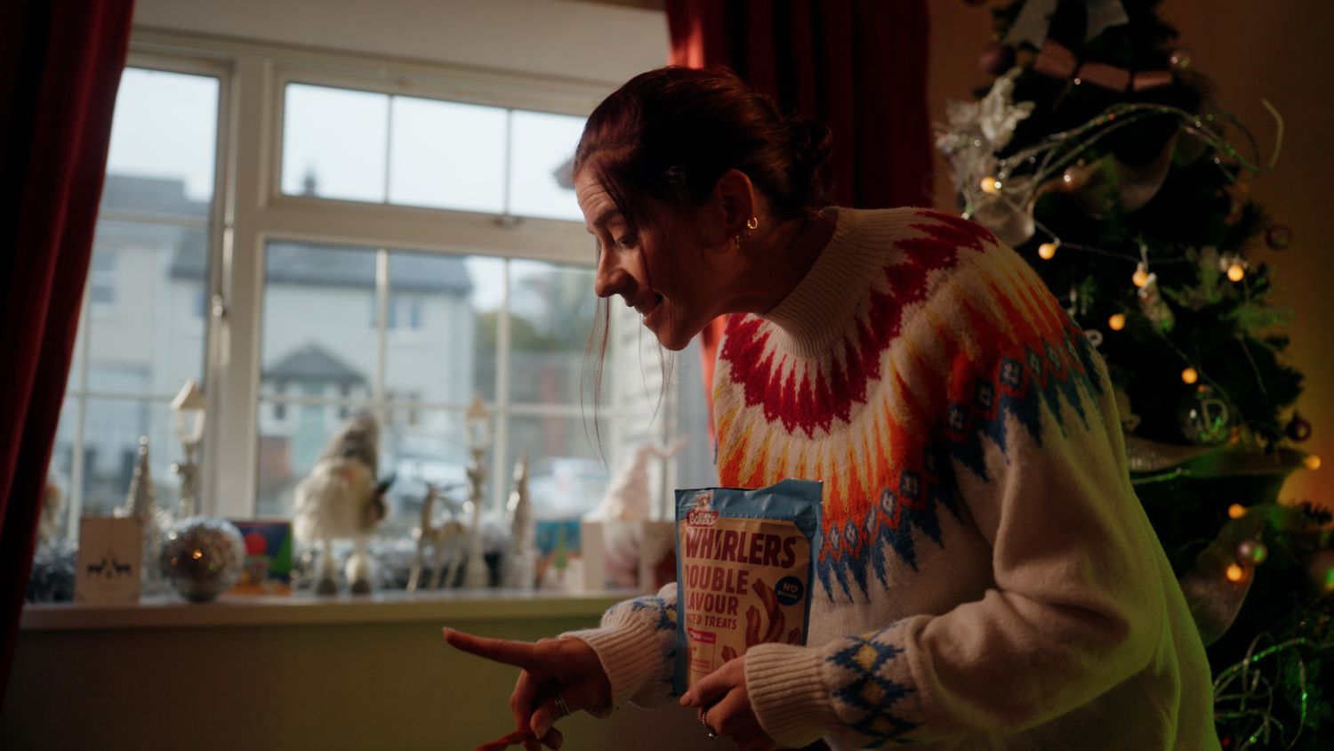 Person in colorful sweater holds magazine near Christmas tree in festive holiday home setting. Nearby Stores, S&W wholesale, TV Advert