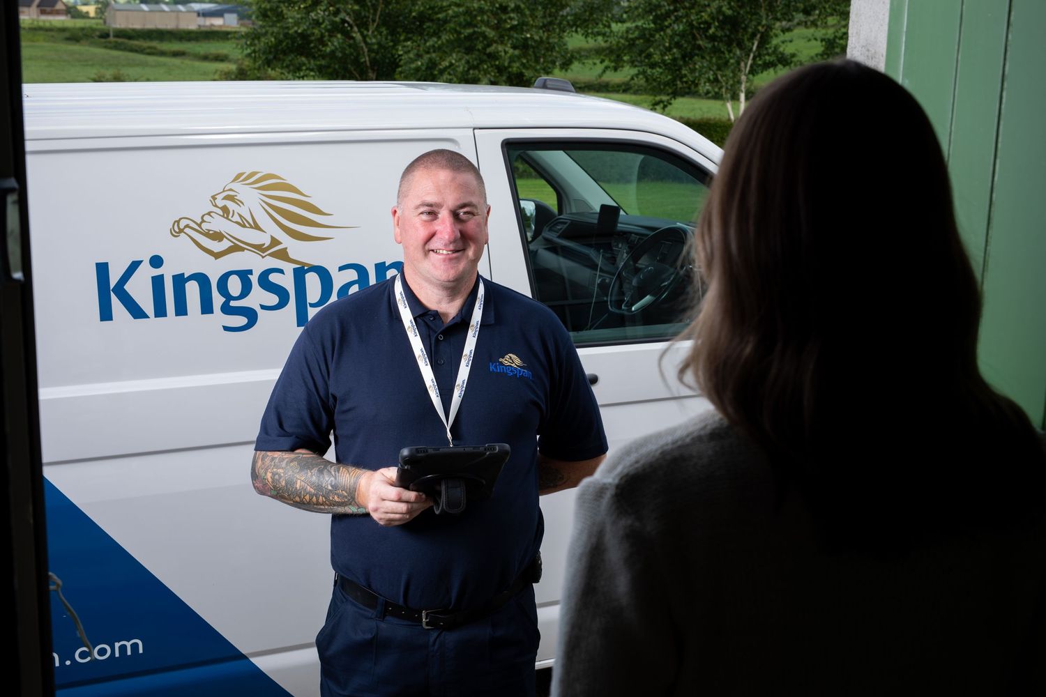 Kingspan engineer smiling at customer doorstep holding tablet next to branded white van. Kingspan Water & Energy