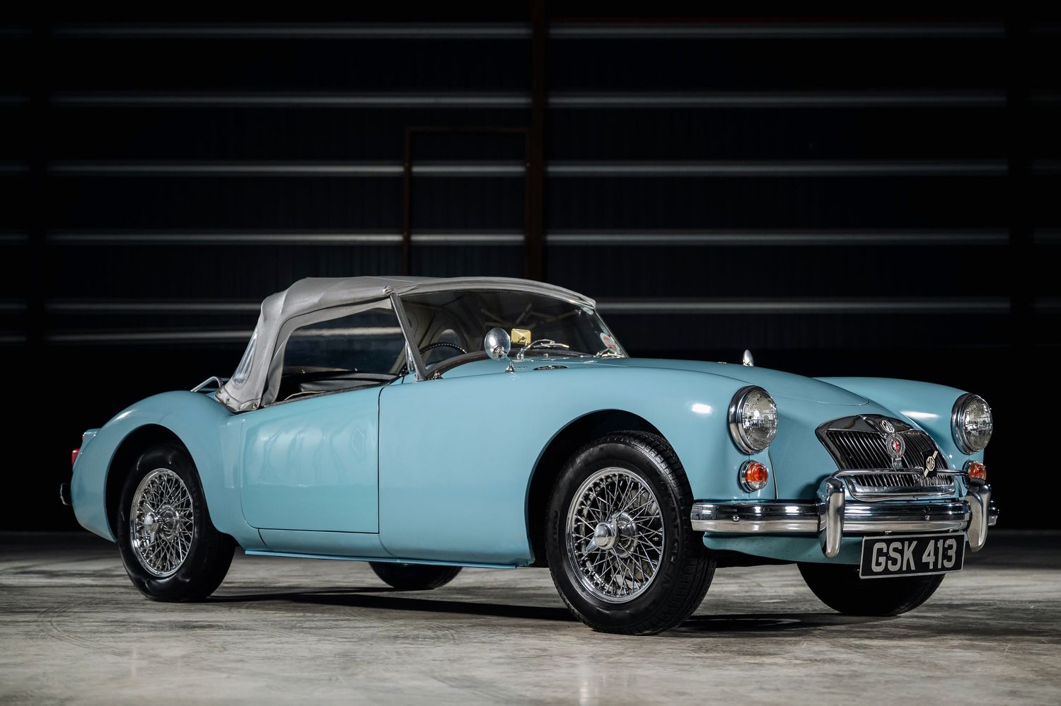 Vintage light blue MGA classic sports car with hardtop and wire wheels in a dark studio setting. The Motorist Collection