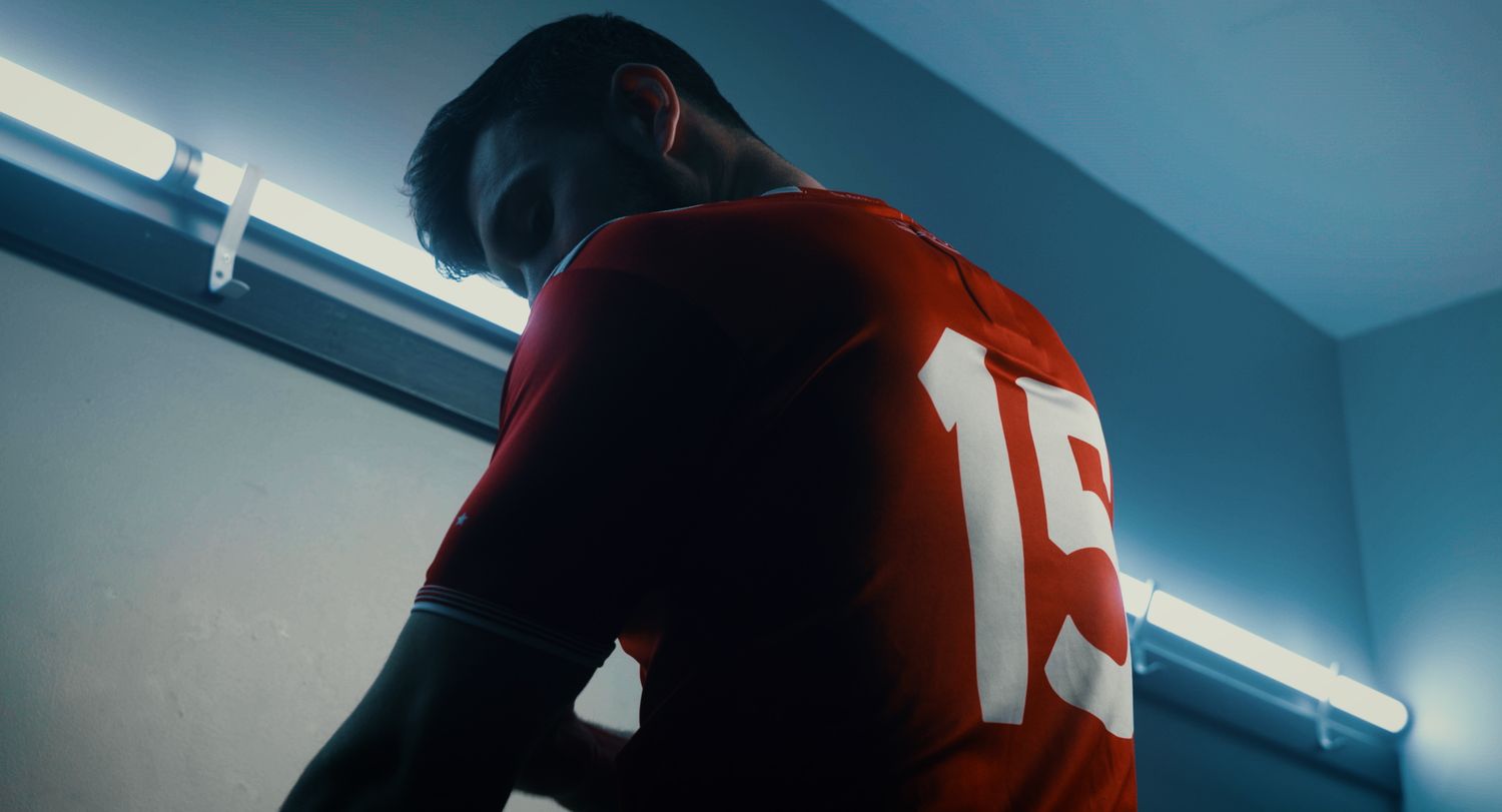 Close-up of athlete in red number 19 jersey leaning forward under fluorescent locker room light. Ulster GAA