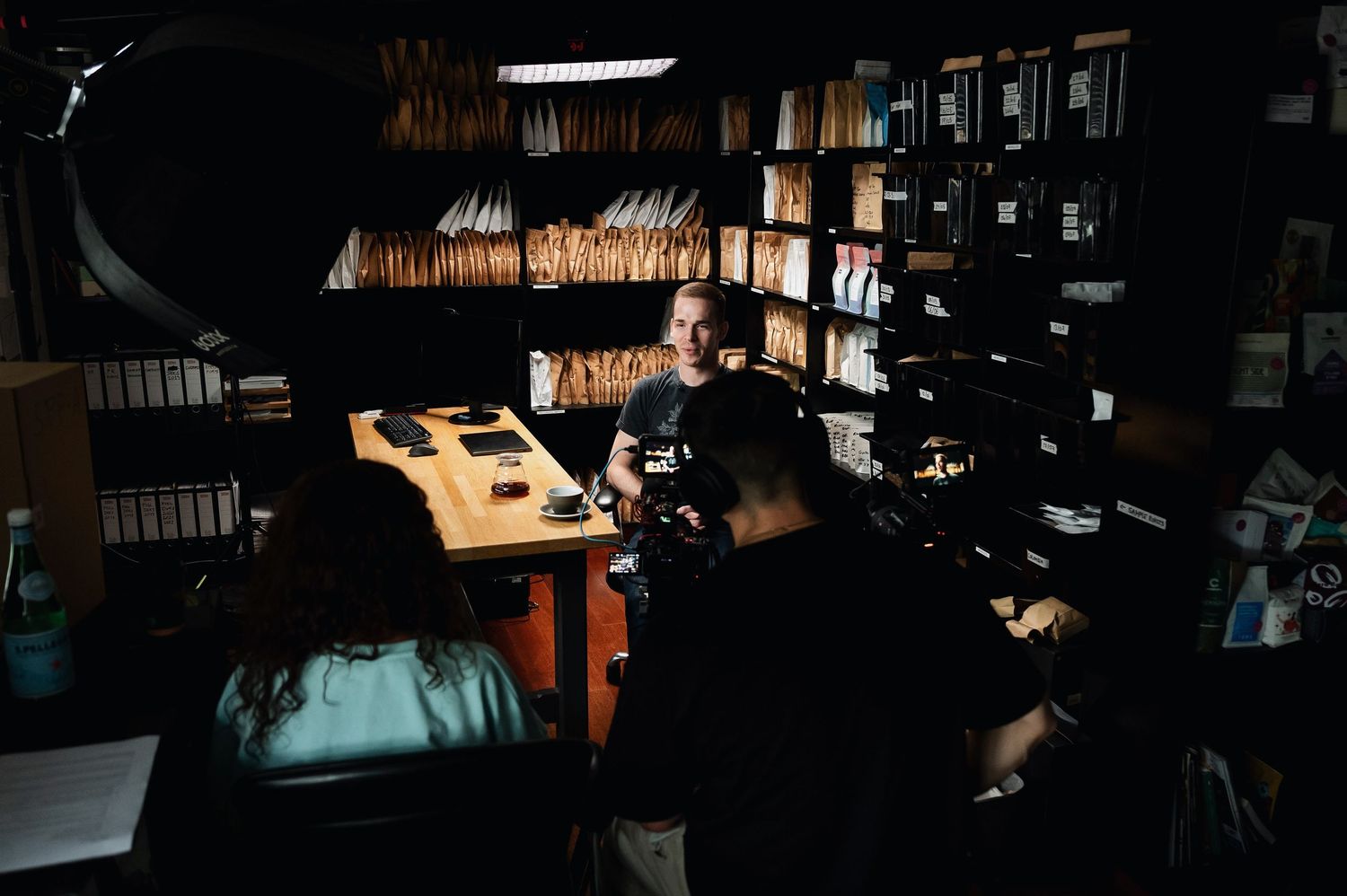 Film crew shooting a documentary scene inside a dimly lit archive room filled with files. Bailies Coffee Roasters