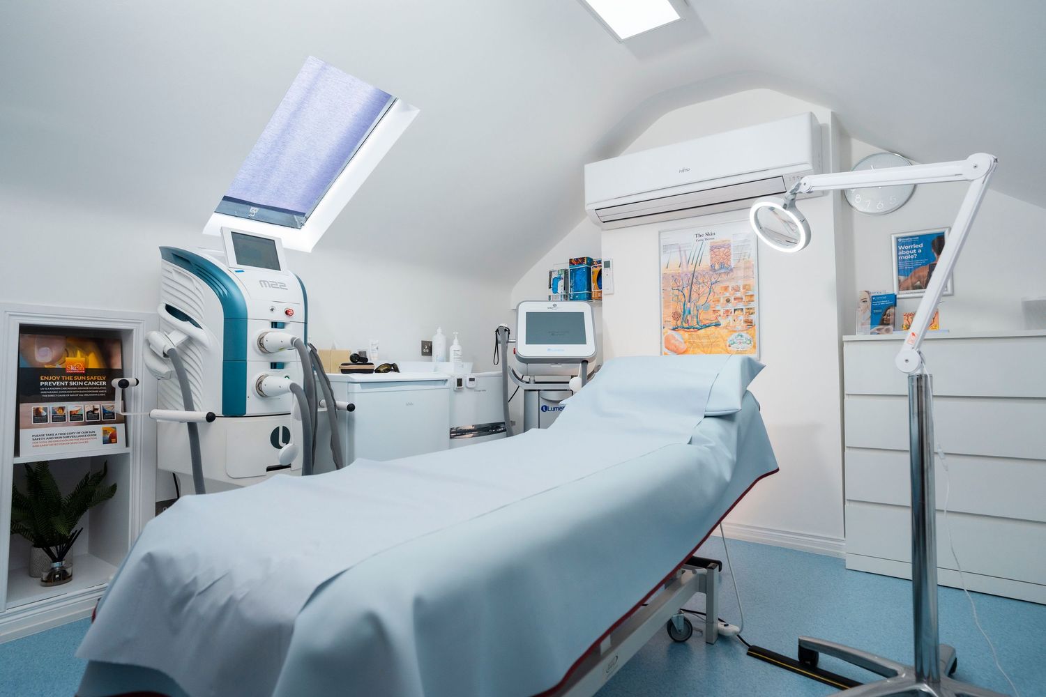 Bright medical treatment room featuring blue examination bed, laser devices and natural skylight. Jenny Flanagan