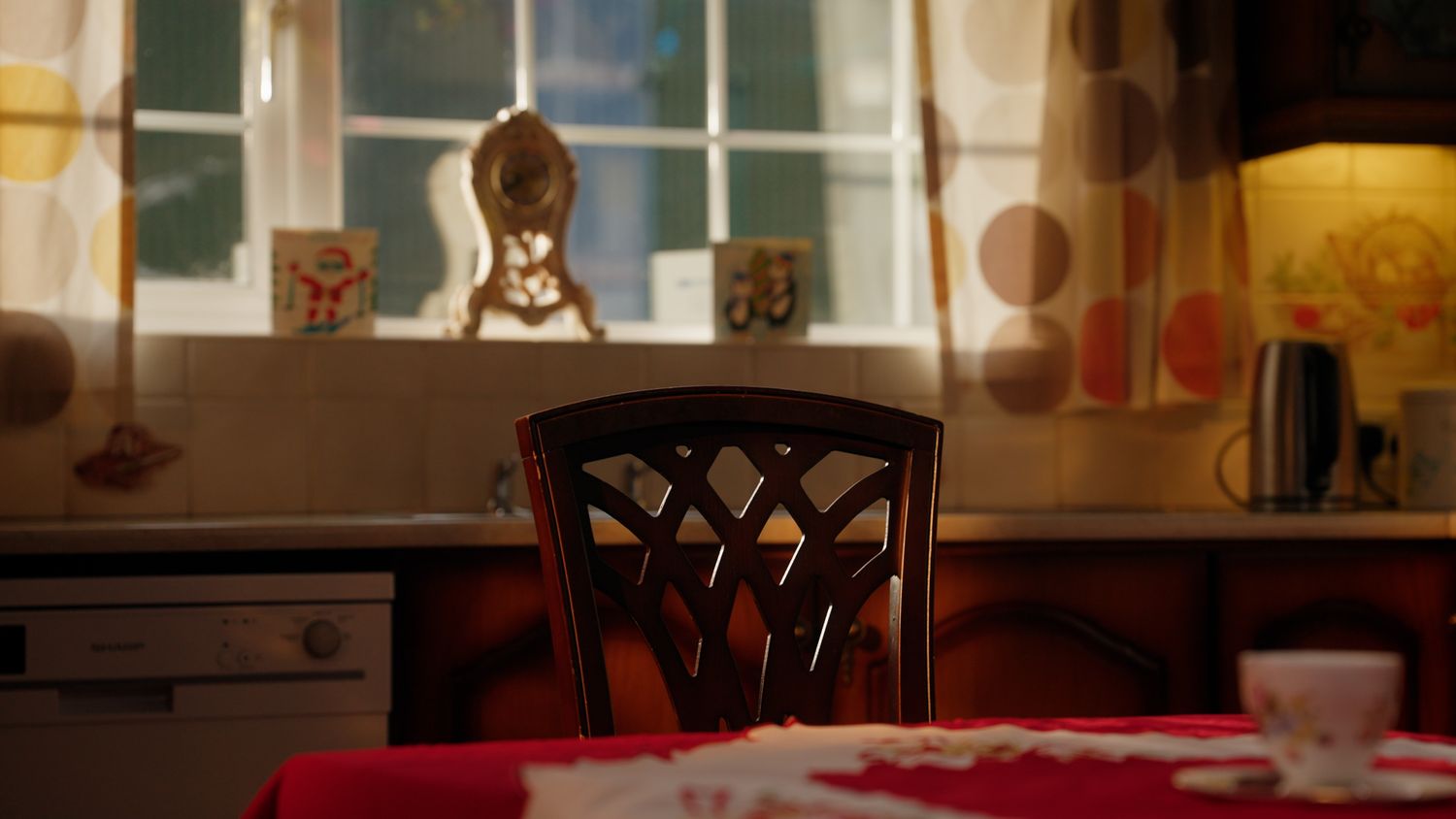 Empty wooden chair at a red tablecloth table in a warm vintage-style Christmas kitchen setting. Nearby Stores, S&W wholesale, TV Advert