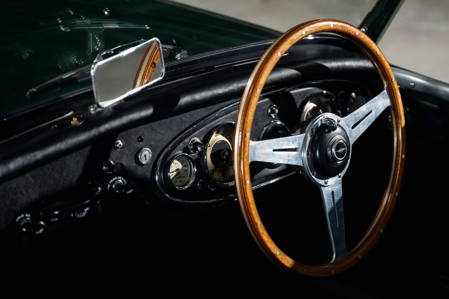 Classic car interior featuring a wooden steering wheel, vintage dashboard gauges, and chrome details in a dark cockpit. Motorist Collection