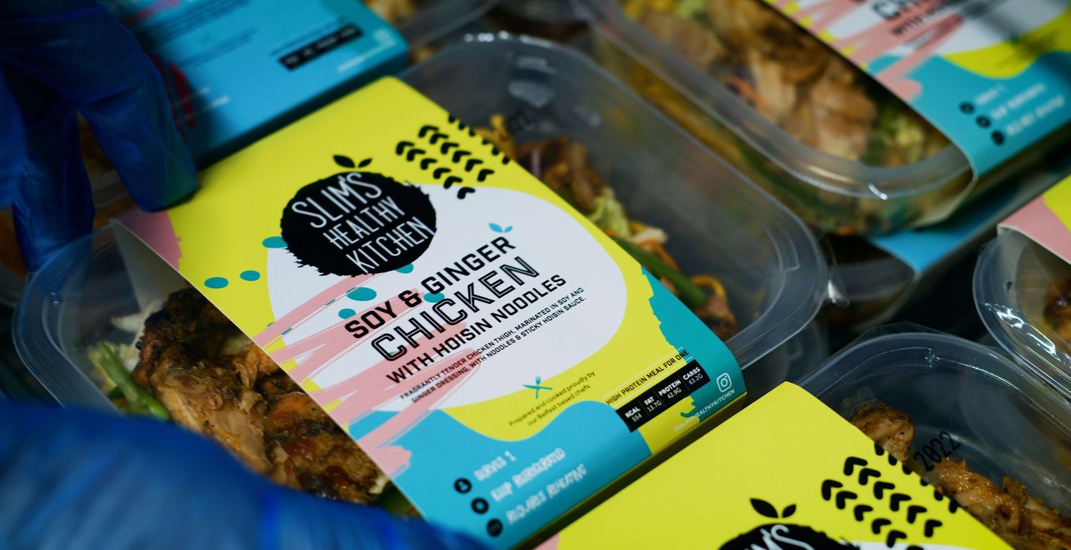 Soy and ginger chicken meal prep container with fresh vegetables and branded packaging on display. Kaizen Brand & Print