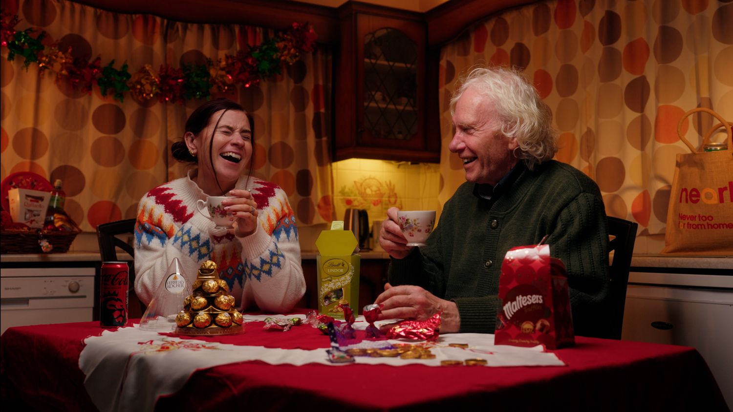 Two people laughing together at a Christmas table with Ferrero Rocher chocolates and festive treats. Nearby Stores, S&W wholesale, TV Advert