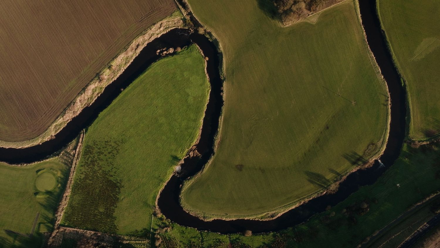 Aerial view of a winding river cutting through lush green farmland fields. Bushmills Whiskey