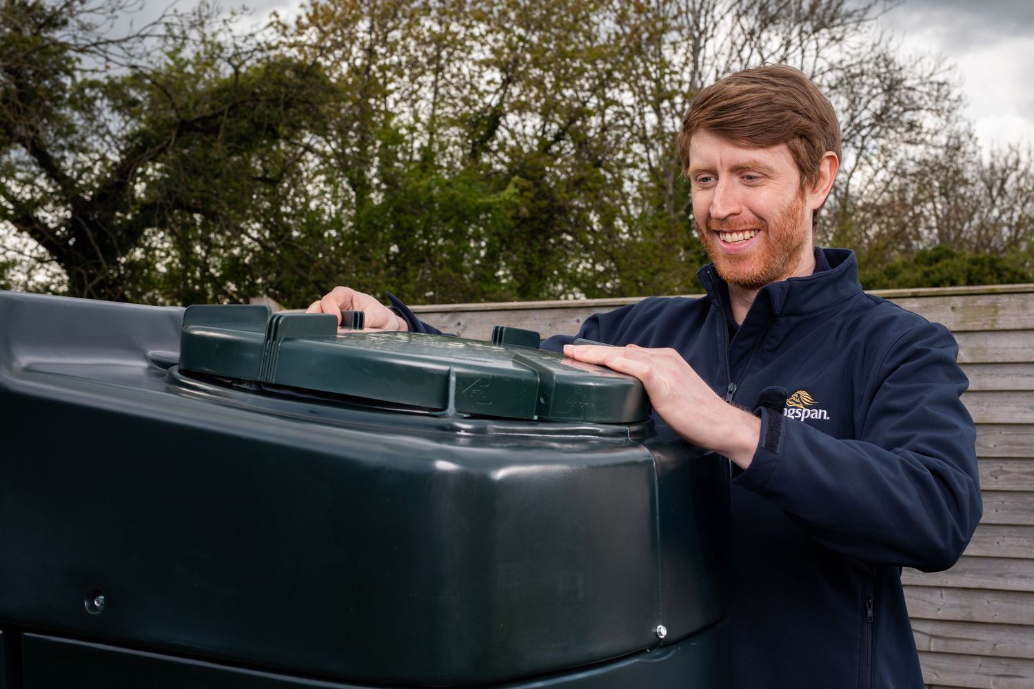 Kingspan technician smiling while checking lid of dark green outdoor oil storage tank. Kingspan Water & Energy