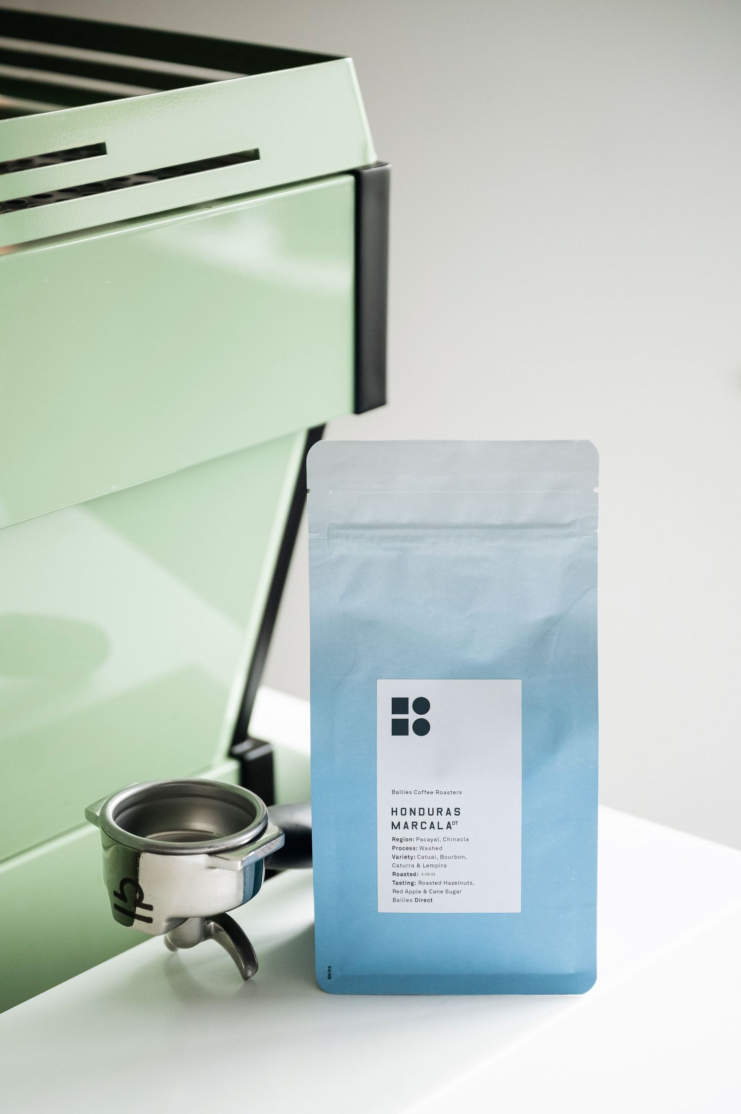 Honduras Marcala specialty coffee bag beside a portafilter against a mint green background. Bailies Coffee Roasters