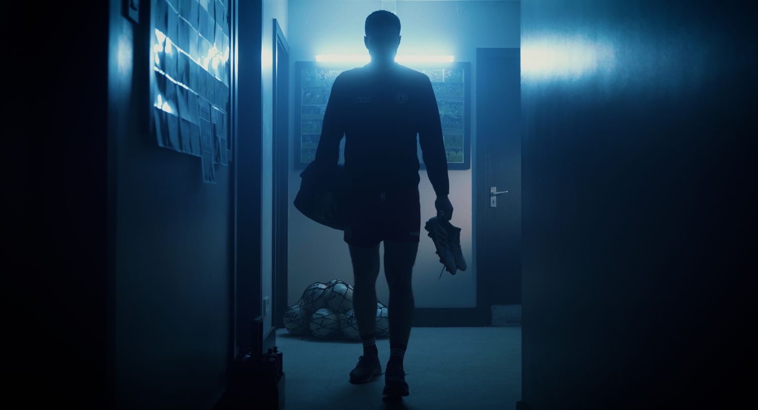 Silhouetted athlete walking down a dark blue-lit hallway carrying a sports bag and shoes. Ulster GAA