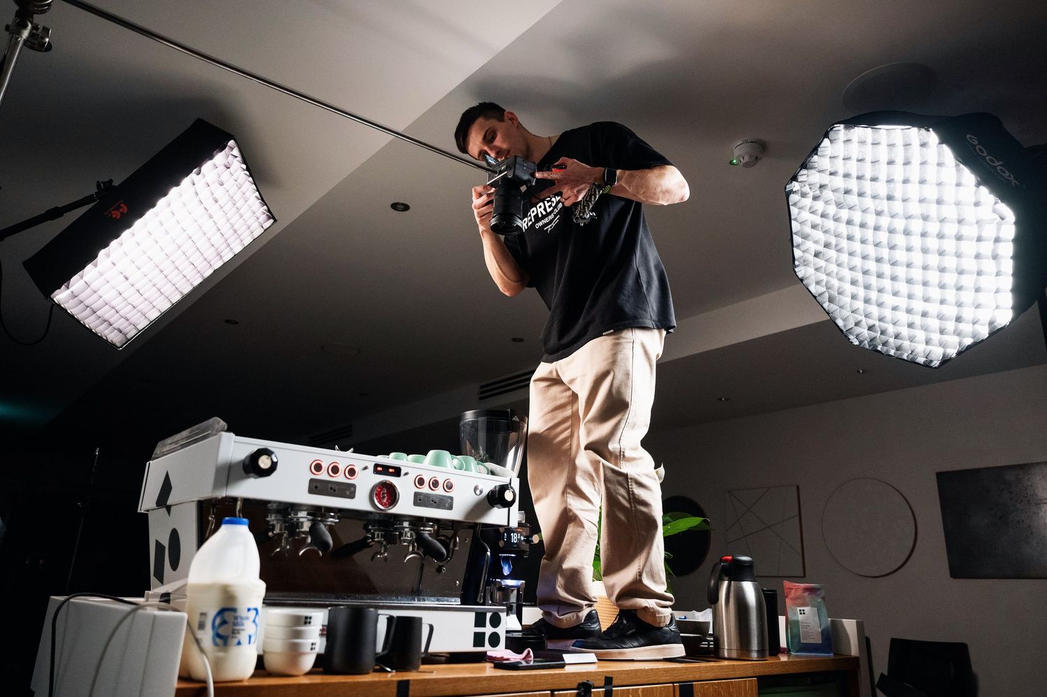 Photographer standing on a table filming a La Marzocco espresso machine under bright studio lights. Bailies Coffee Roasters