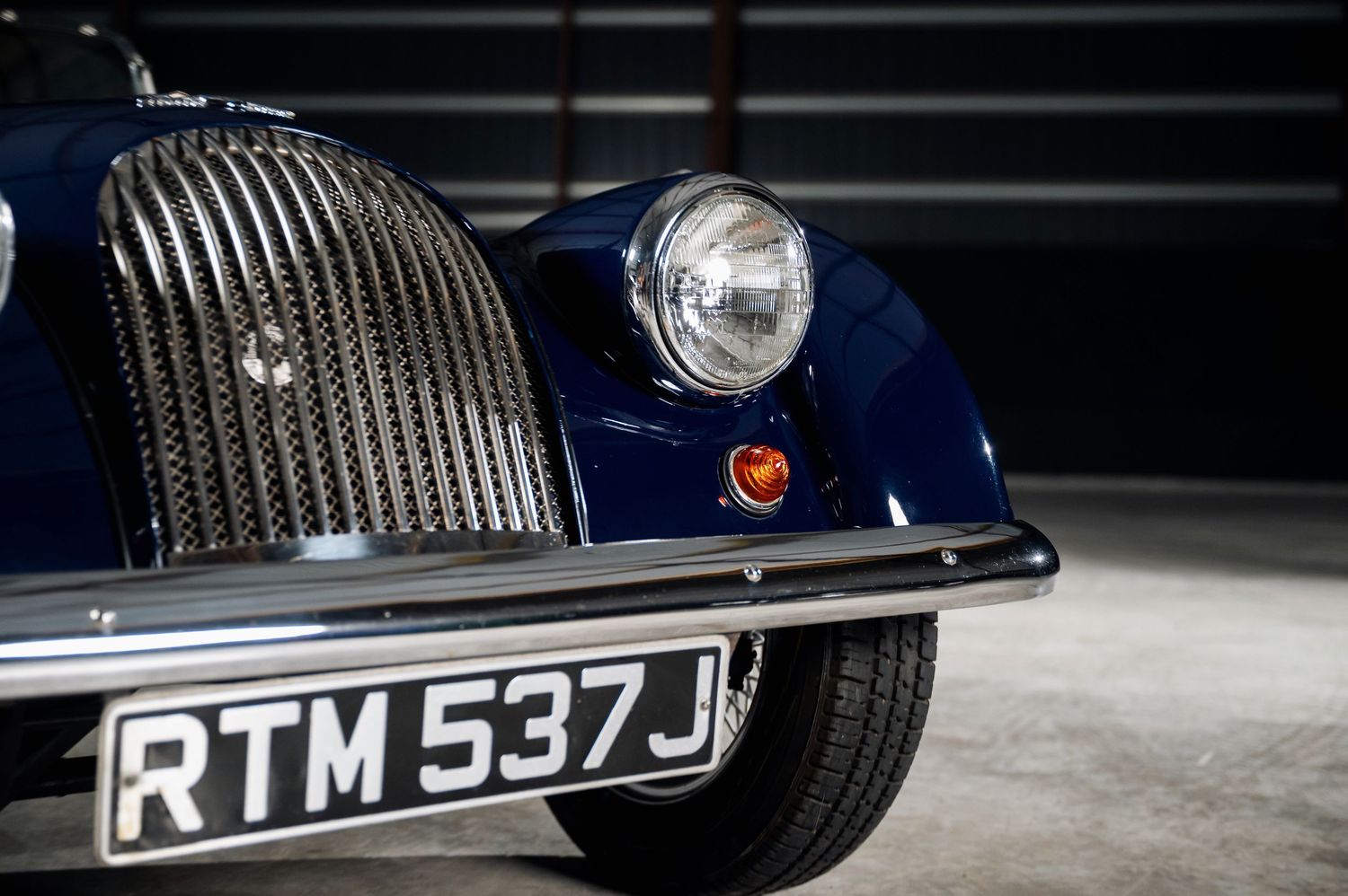 Close-up of navy blue classic car front grille and headlight with registration plate. Motorist Collection