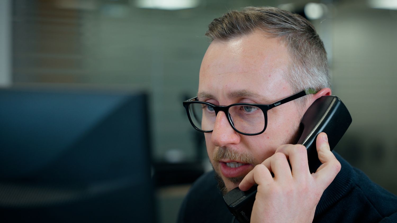 Man with glasses talking on a smartphone while sitting at an office desk. Briggs Equipment