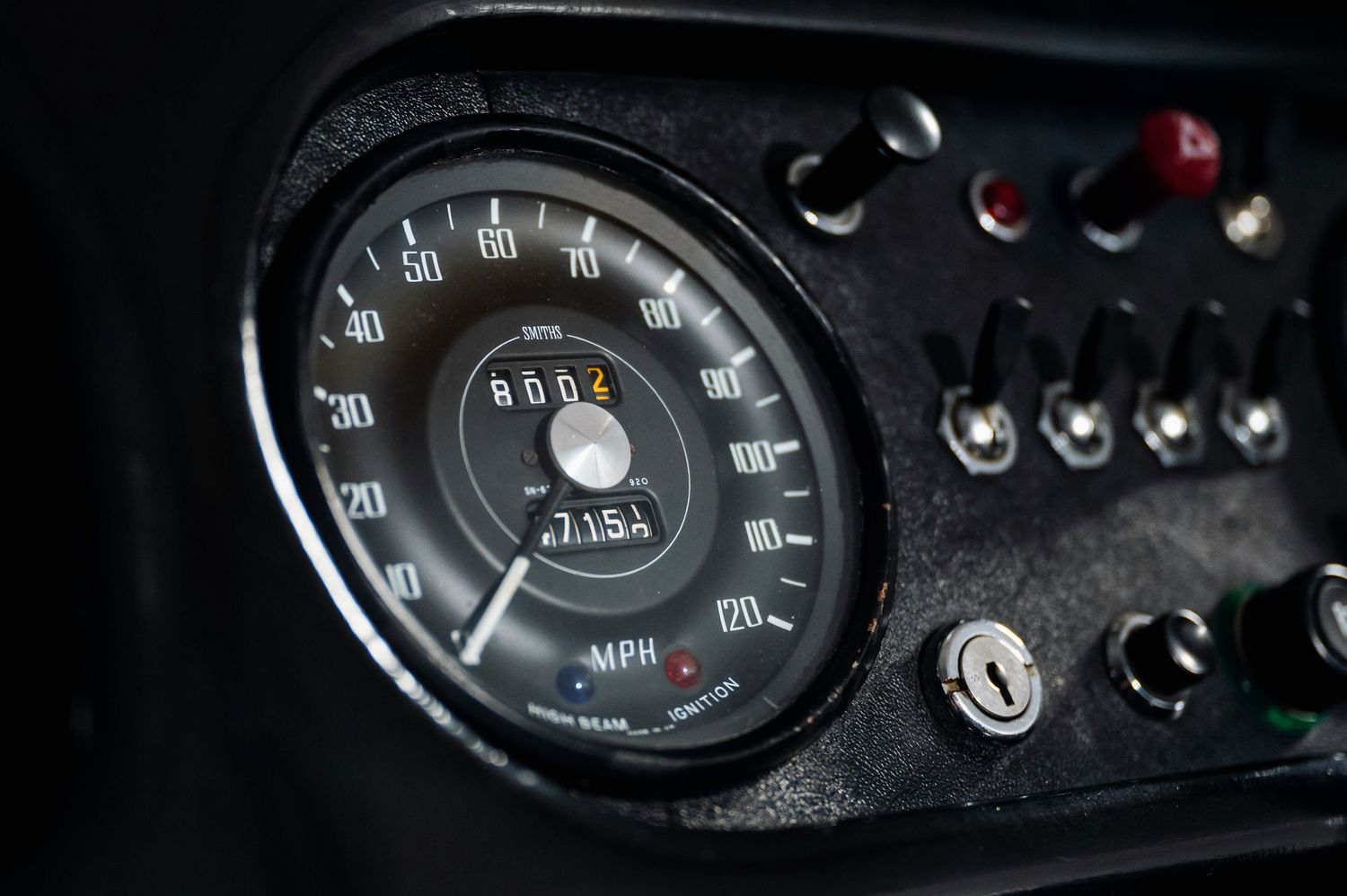 Classic car speedometer gauge showing MPH reading with ignition switch on dark dashboard panel. Motorist Collection