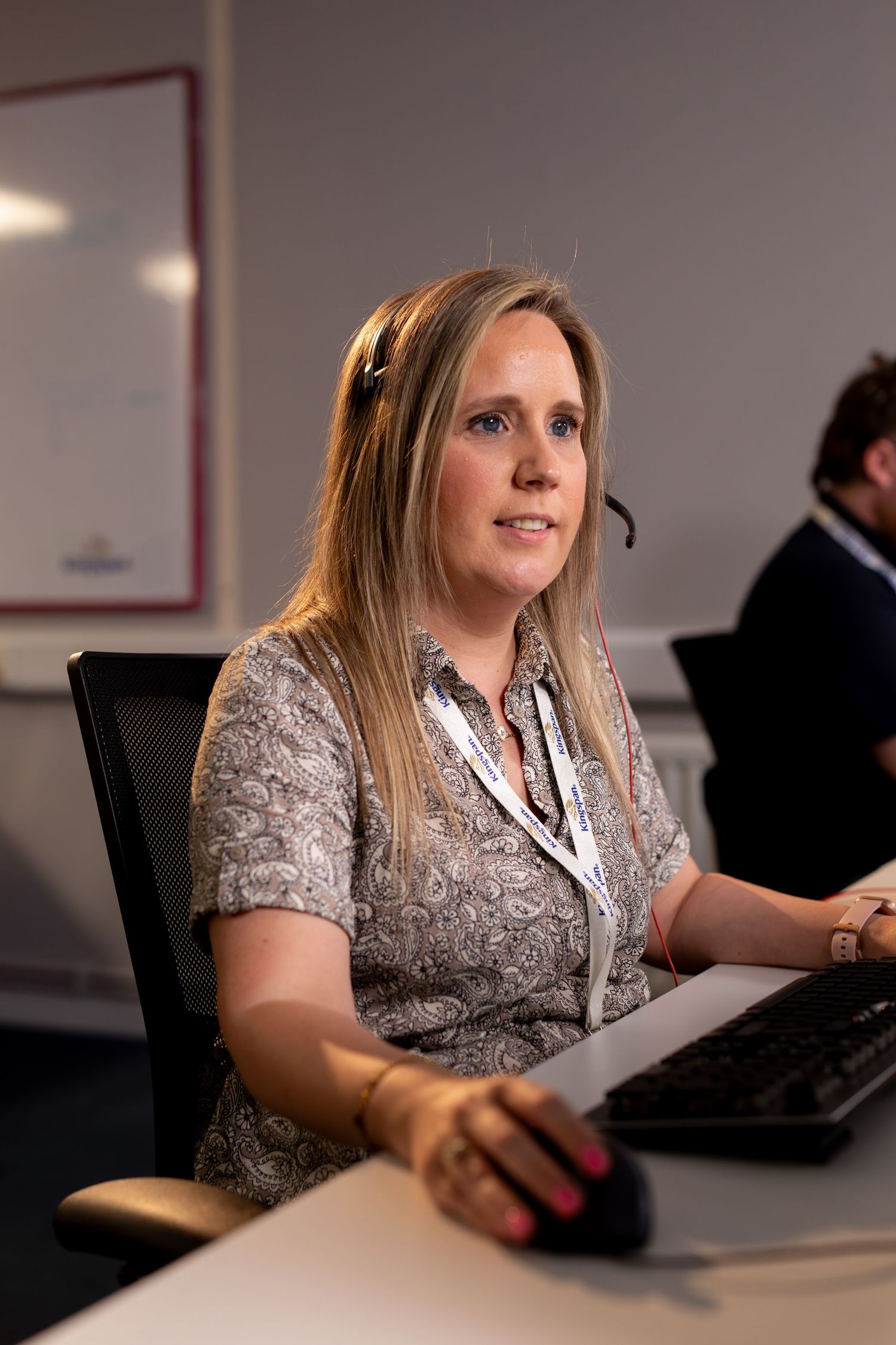Female call center agent wearing headset and lanyard working at computer desk in office. Kingspan Water & Energy
