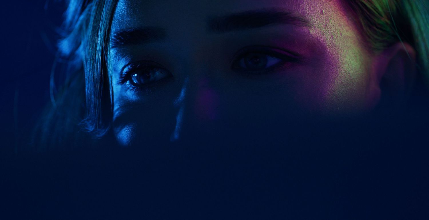 Close-up portrait of a woman with blue and pink neon lighting illuminating her face in darkness. Kaizen Brand & Print