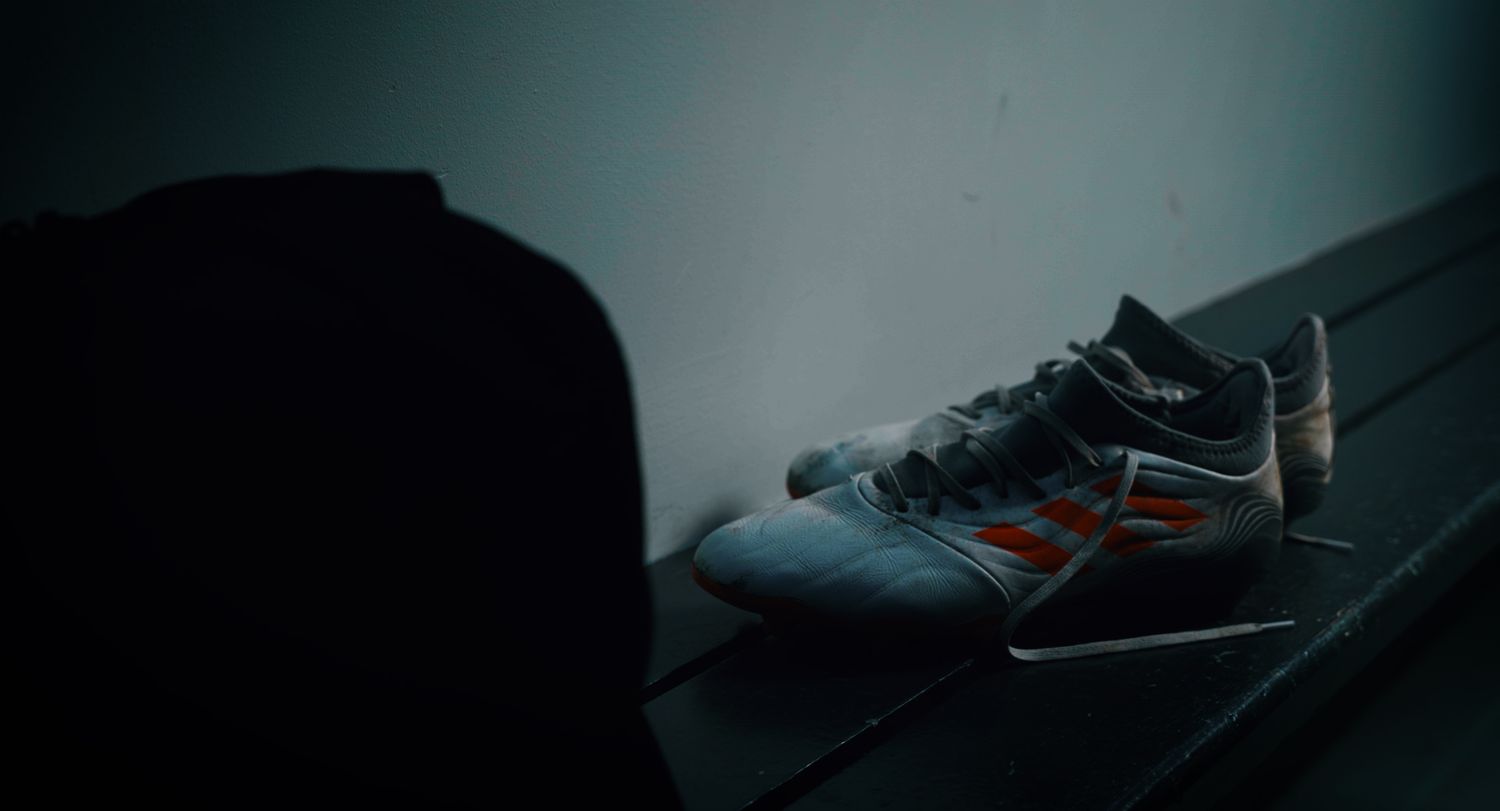 A pair of Adidas football boots resting on a bench in a dark locker room. Ulster GAA