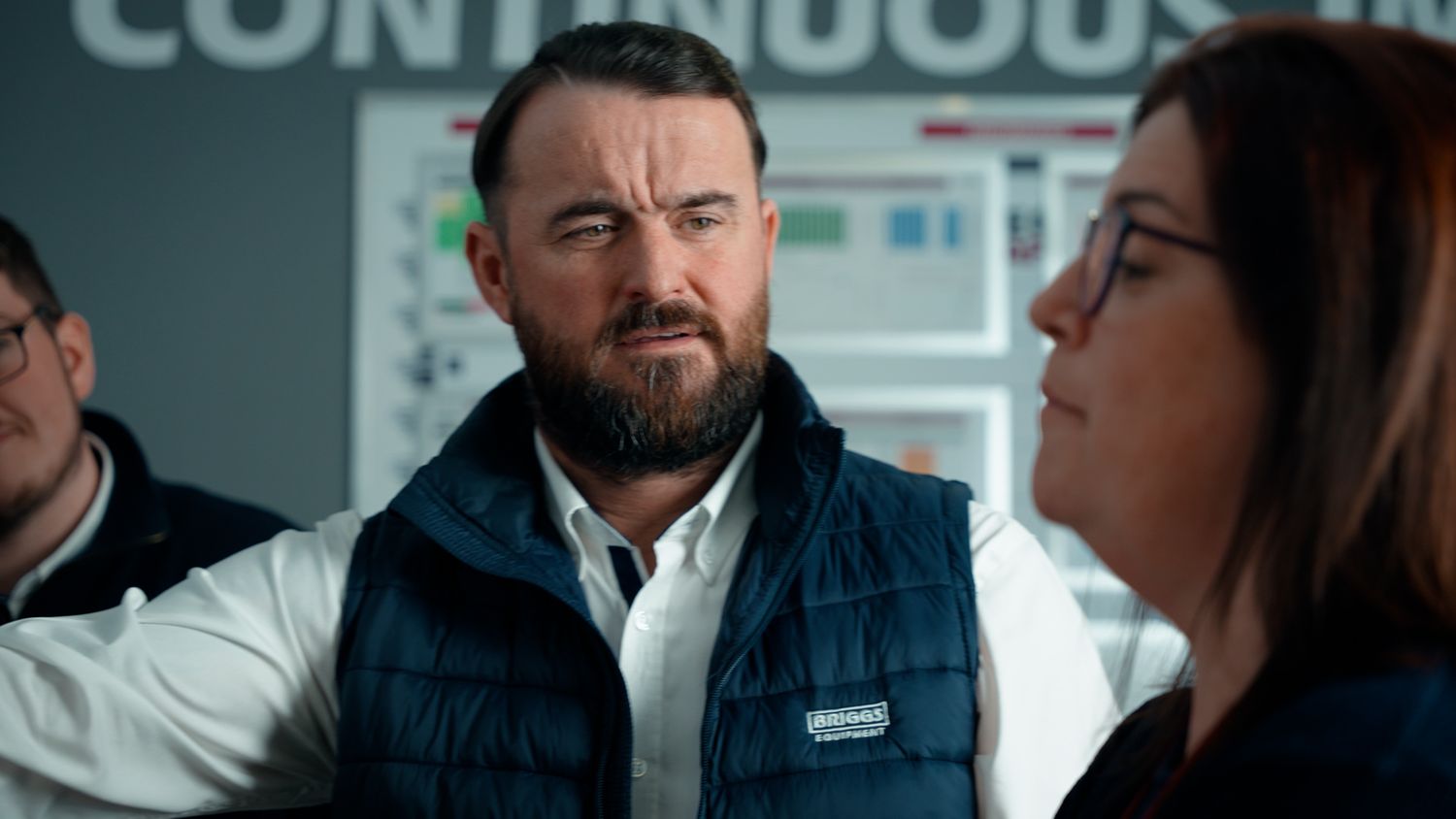Man in a navy quilted vest listening attentively during a workplace meeting. Briggs Equipment