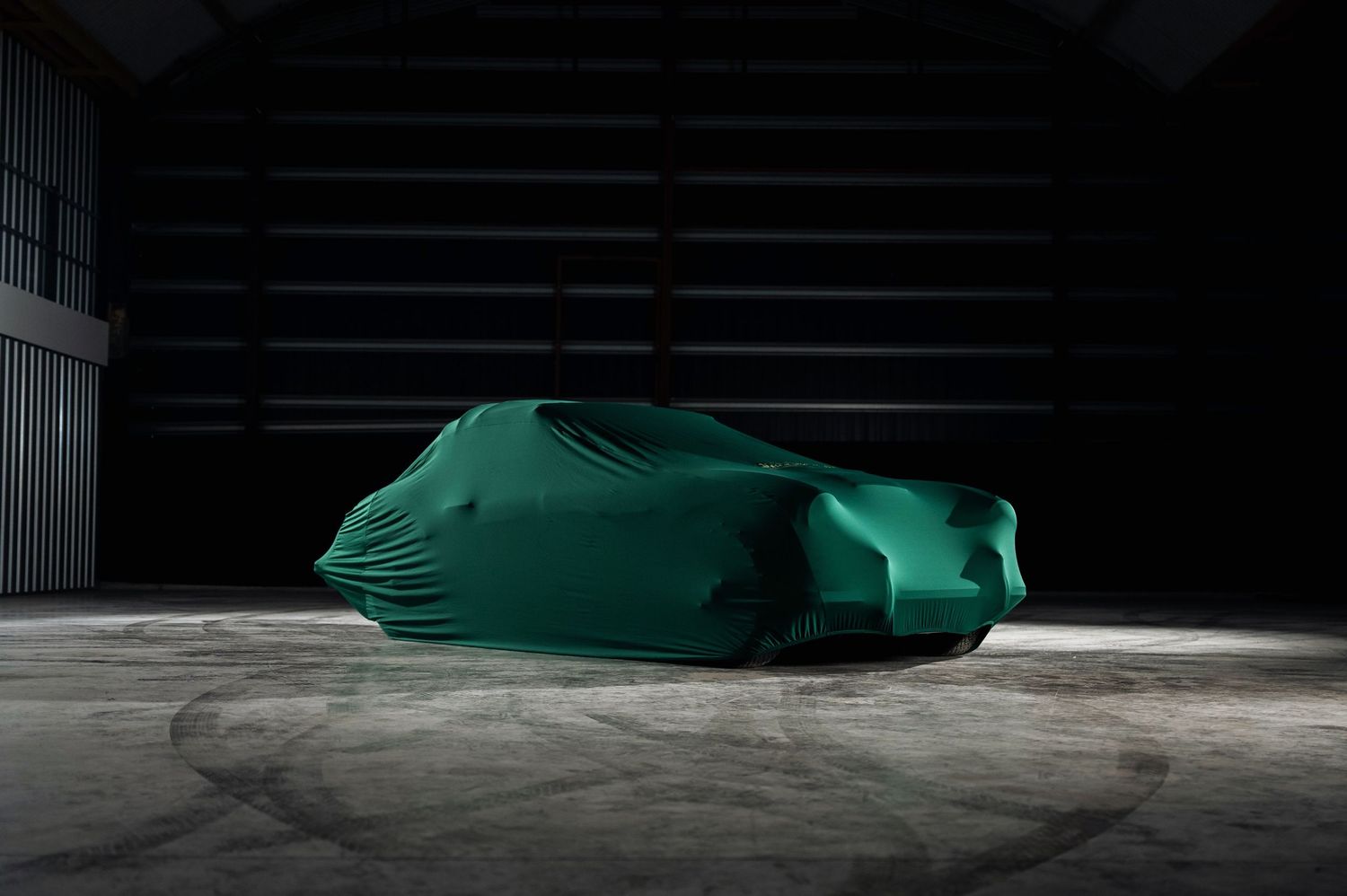 A mysterious green car cover draped over a vehicle in a dark dramatic garage setting. Motorist Collection