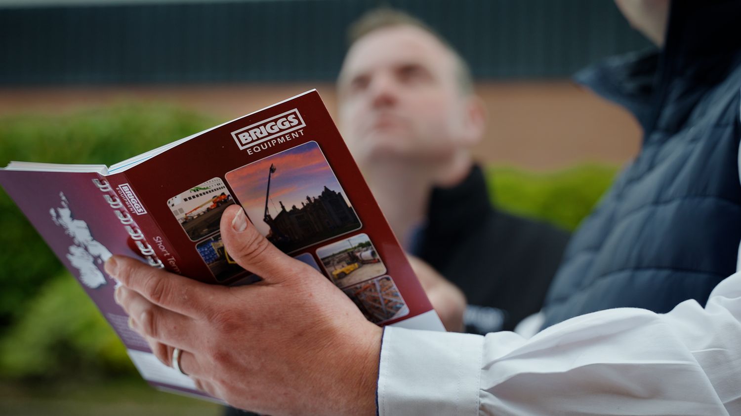 Person reading a Briggs equipment catalog outdoors at an industrial machinery dealership event.