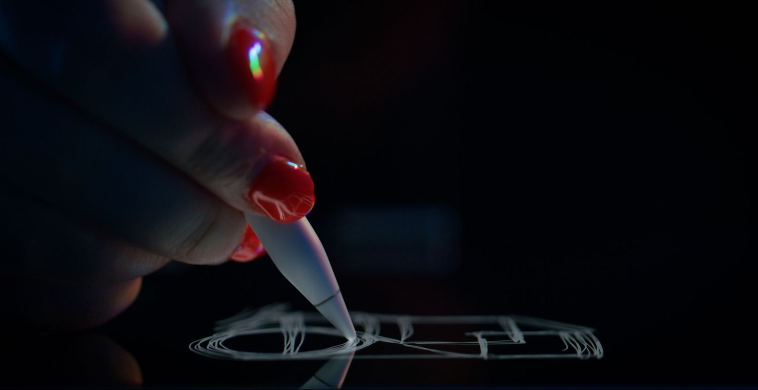 Close-up of red-nailed fingers using a stylus pen to sketch a phone design on a dark surface. Kaizen Brand & Print