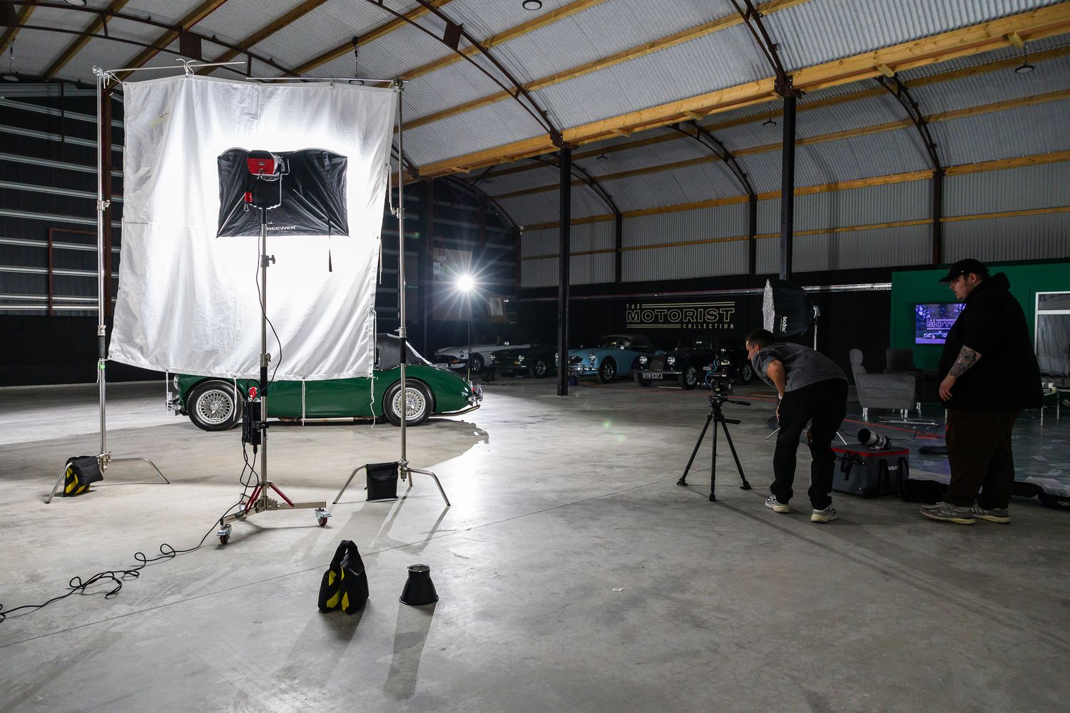 Photographers set up professional lighting equipment inside a large industrial warehouse for a photo shoot.
