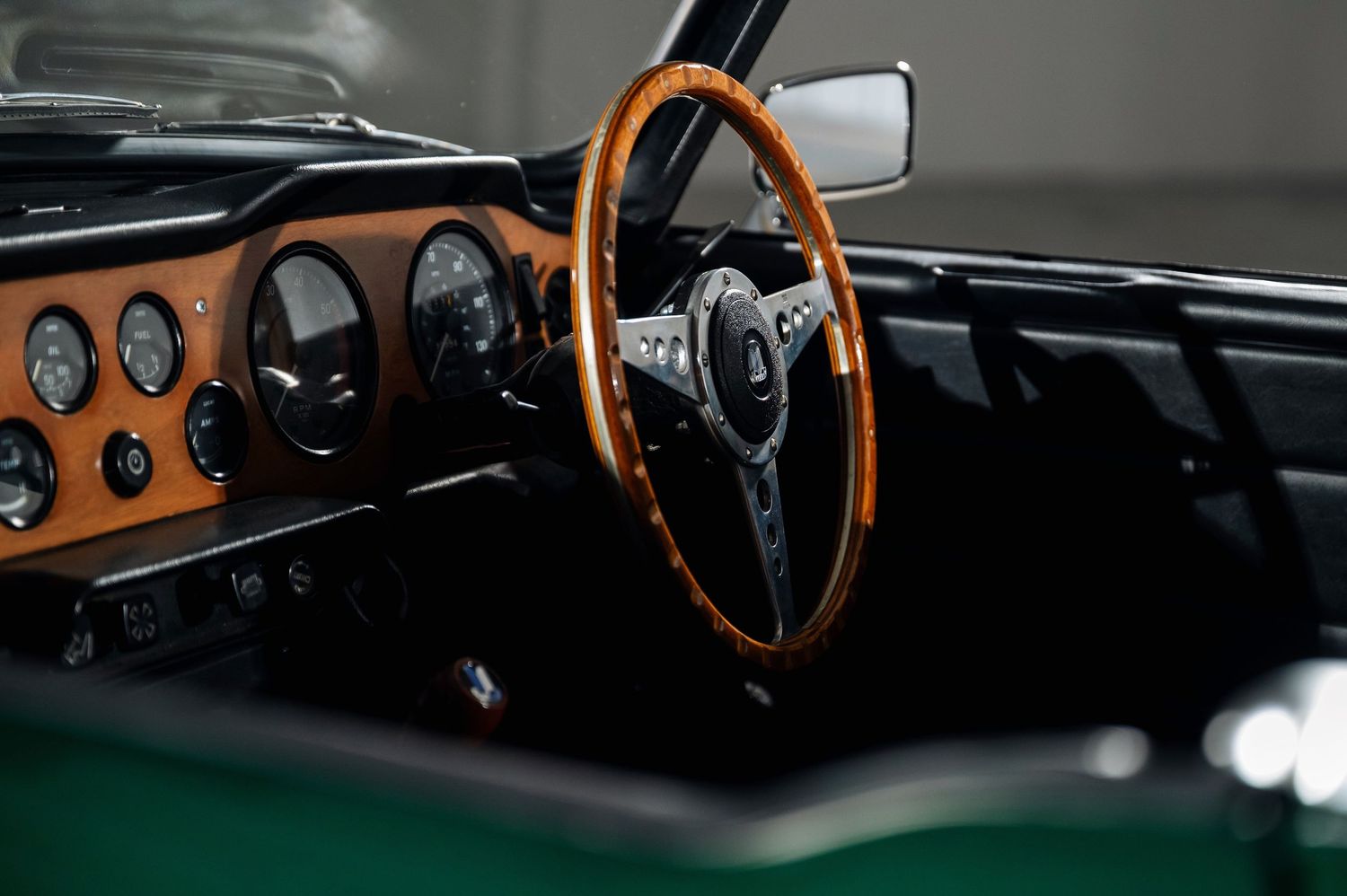 Vintage Triumph TR6 interior showcasing a wooden steering wheel, walnut dashboard, and classic analog instrument gauges. Motorist Collection