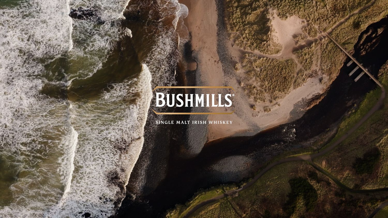 Aerial view of Irish coastline with Bushmills Single Malt Irish Whiskey branding overlay. Bushmills Whiskey