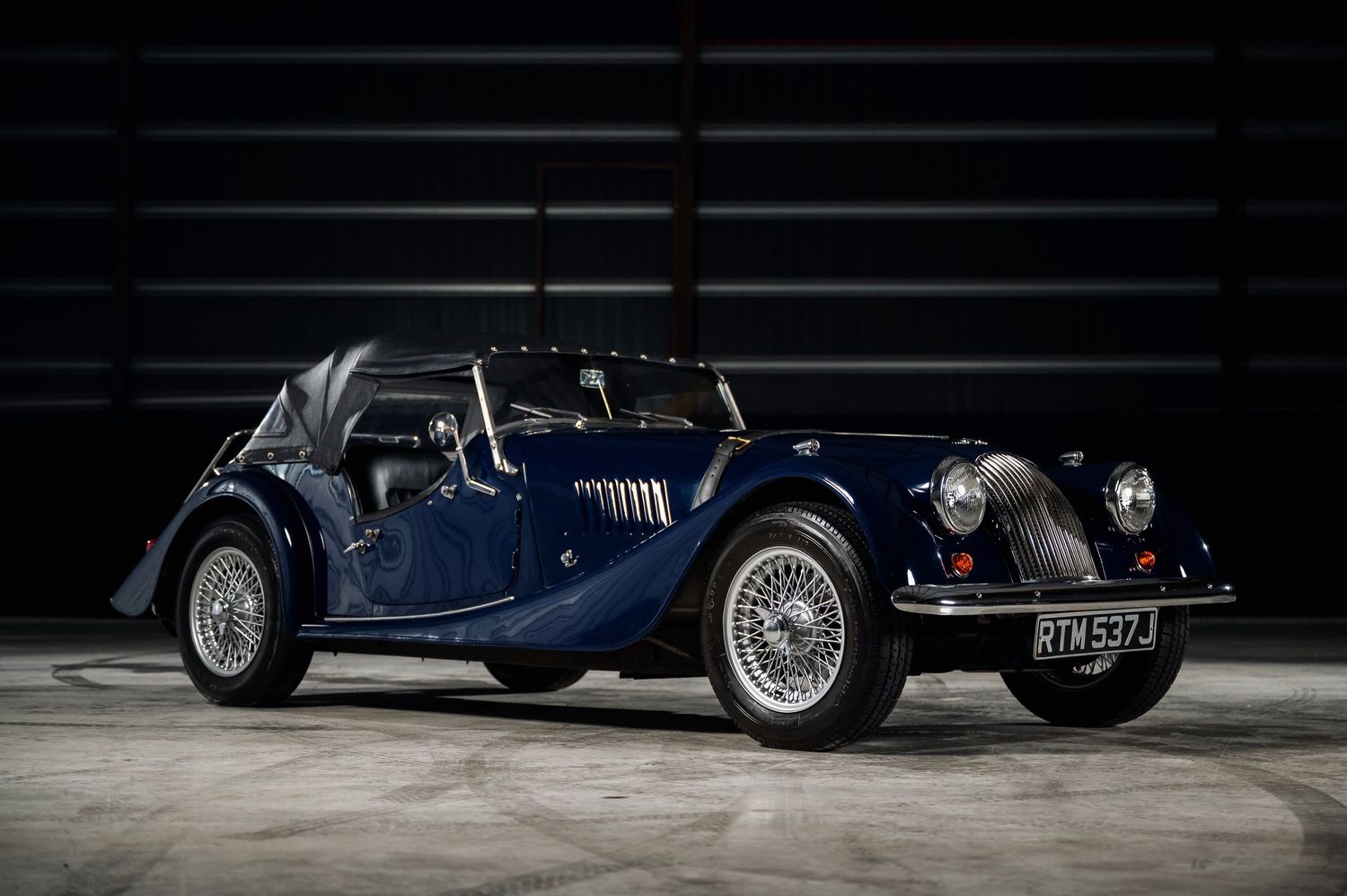 Classic navy blue Morgan 4/4 vintage roadster with wire wheels photographed in a dark studio environment. The Motorist Collection