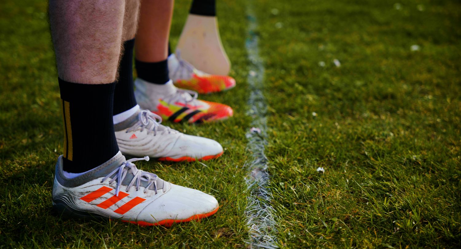Row of players wearing Adidas football boots standing on a grass pitch sideline. Ulster GAA