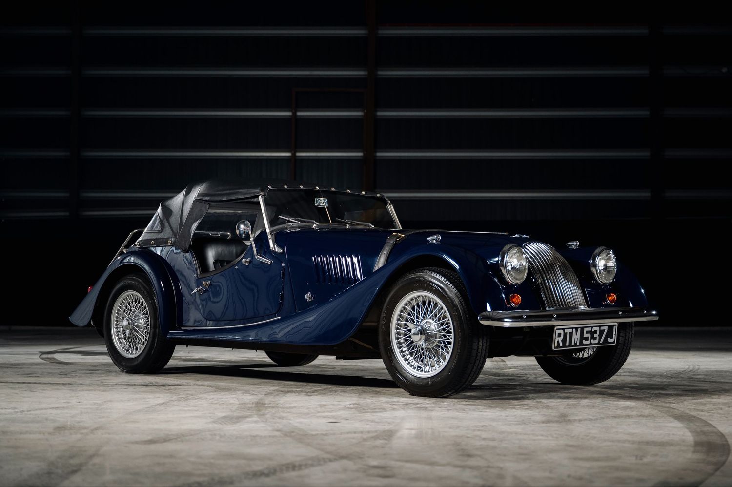 Navy blue Morgan classic sports car with wire wheels and convertible top, parked indoors. Motorist Collection