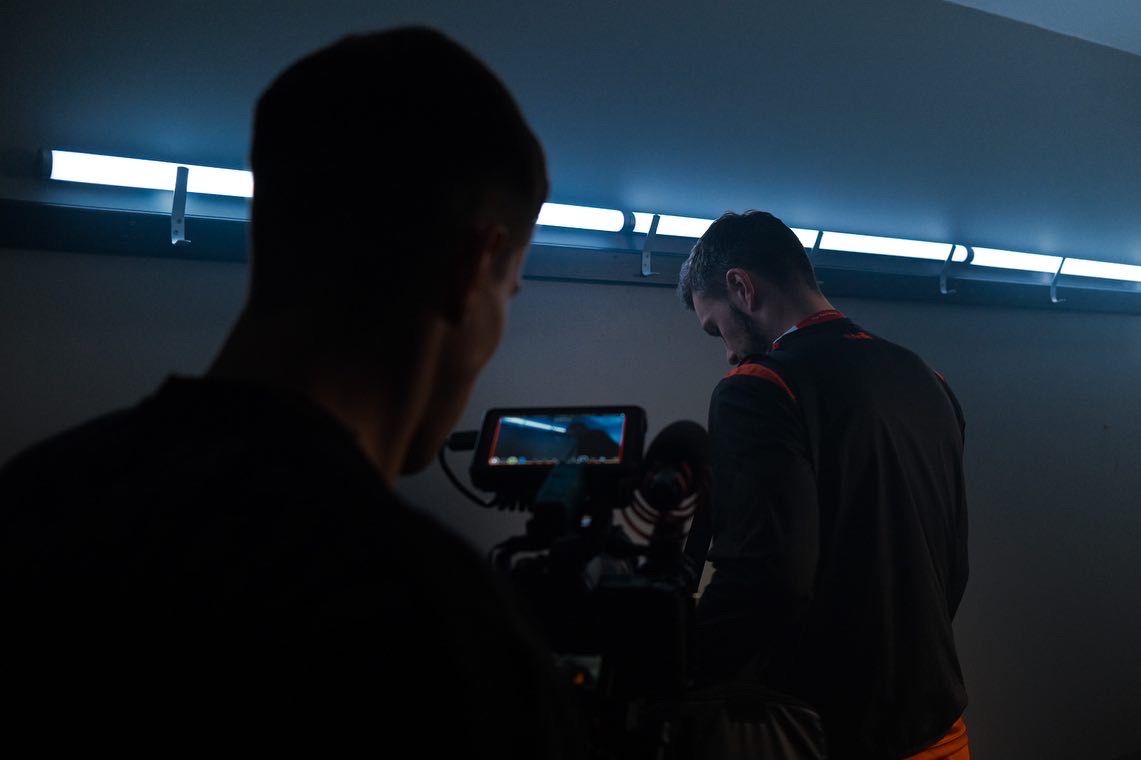 Two filmmakers work with professional camera equipment in a dark studio with blue neon lighting. Ulster GAA