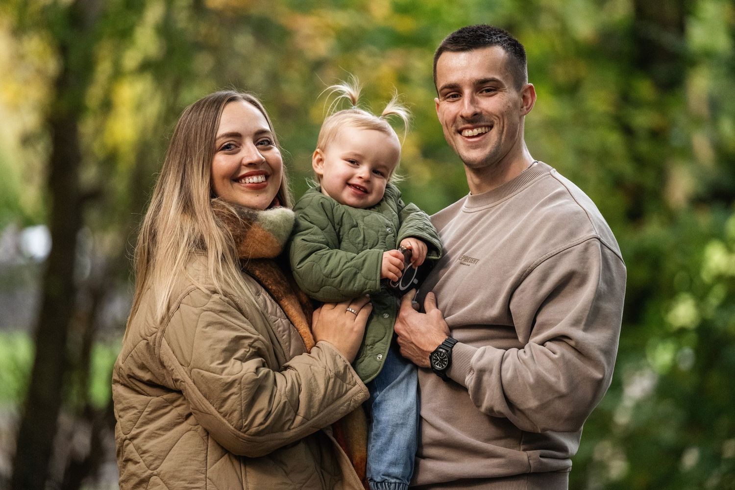 Happy young family with a smiling toddler posing together in an autumn park with colorful foliage.