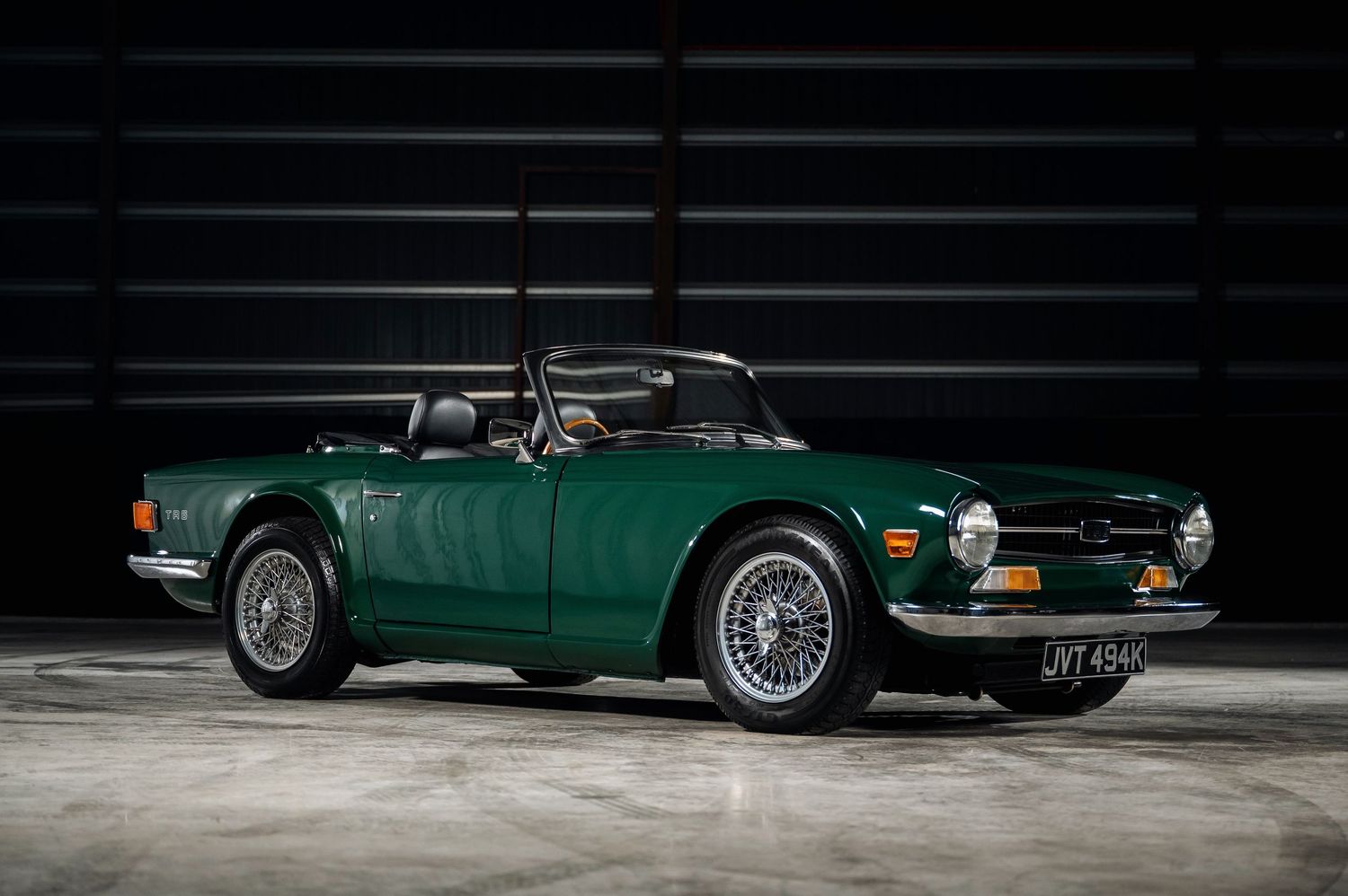 Classic green Triumph TR6 convertible sports car with wire wheels photographed in a dark studio setting.