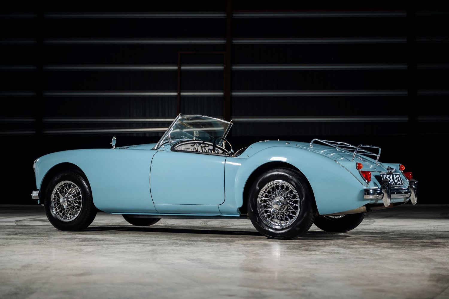 Rear three-quarter view of a light blue MGA classic convertible sports car with chrome luggage rack. Motorist Collection