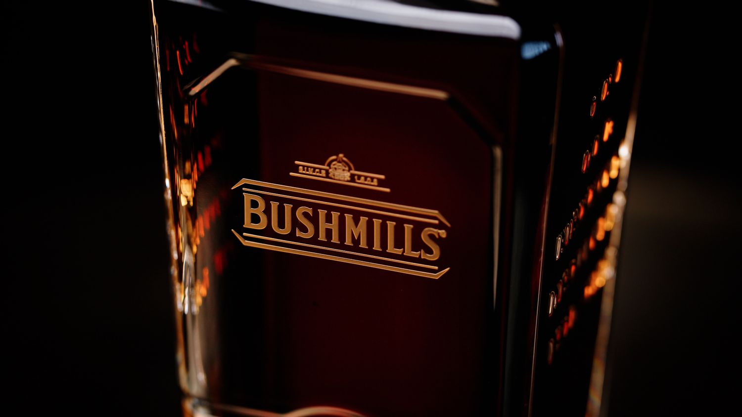 Close-up of a Bushmills Irish whiskey glass with engraved logo on dark background. Bushmills Whiskey
