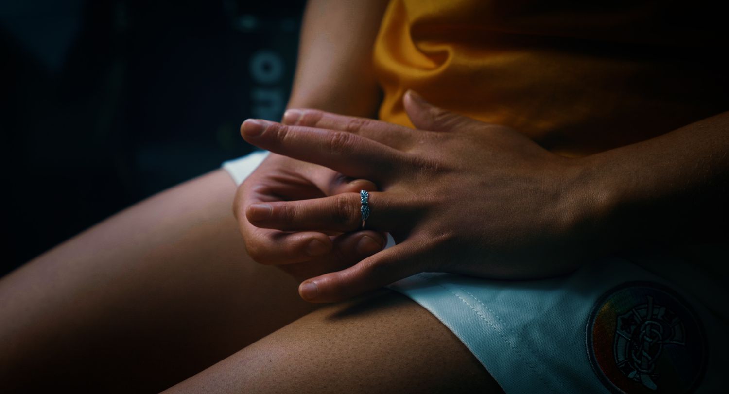 Close-up of hands with rings resting on knees wearing a yellow sports outfit. Ulster GAA