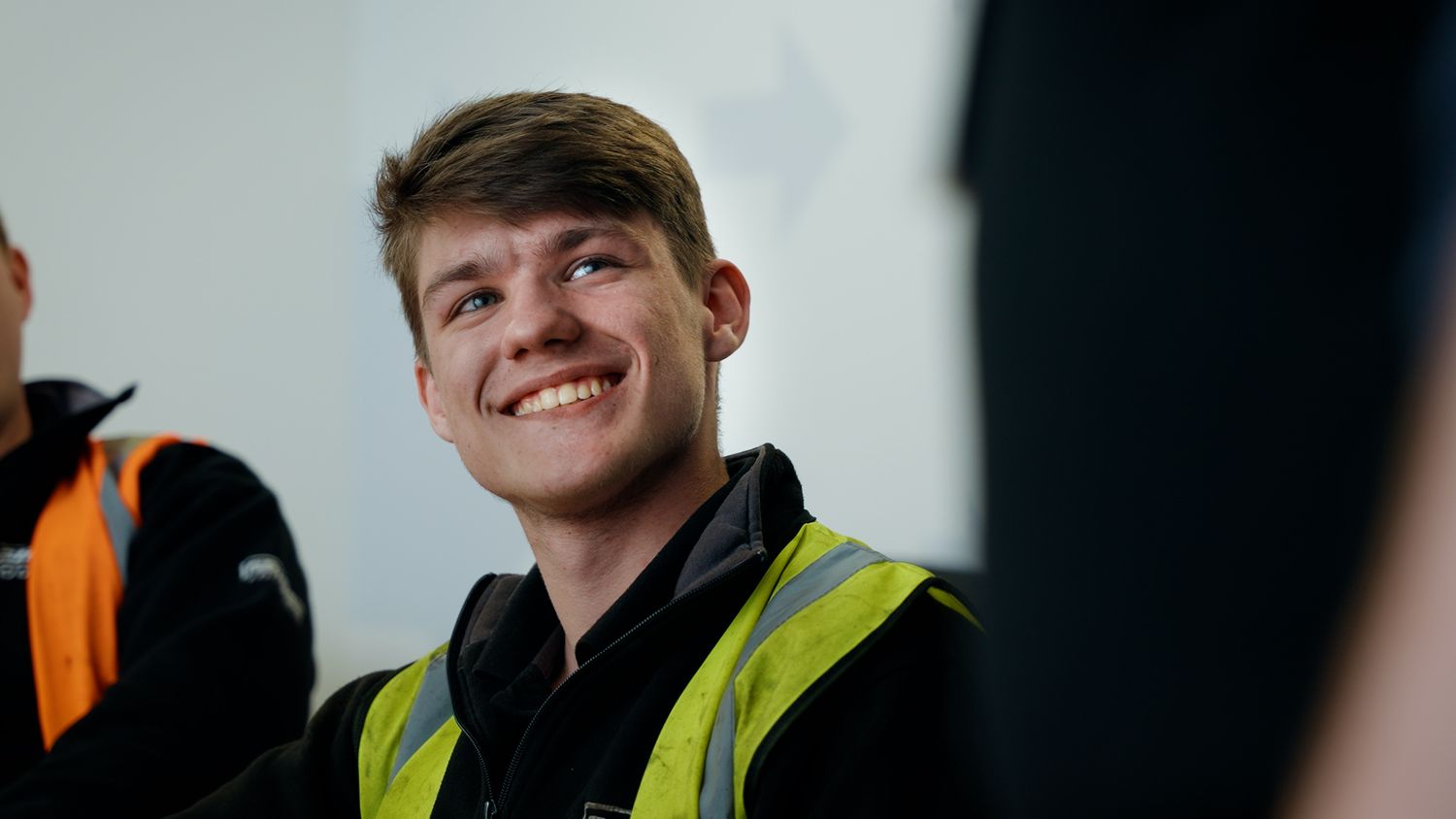 Smiling young man wearing a yellow high-visibility vest in a workplace environment. Briggs Equipment