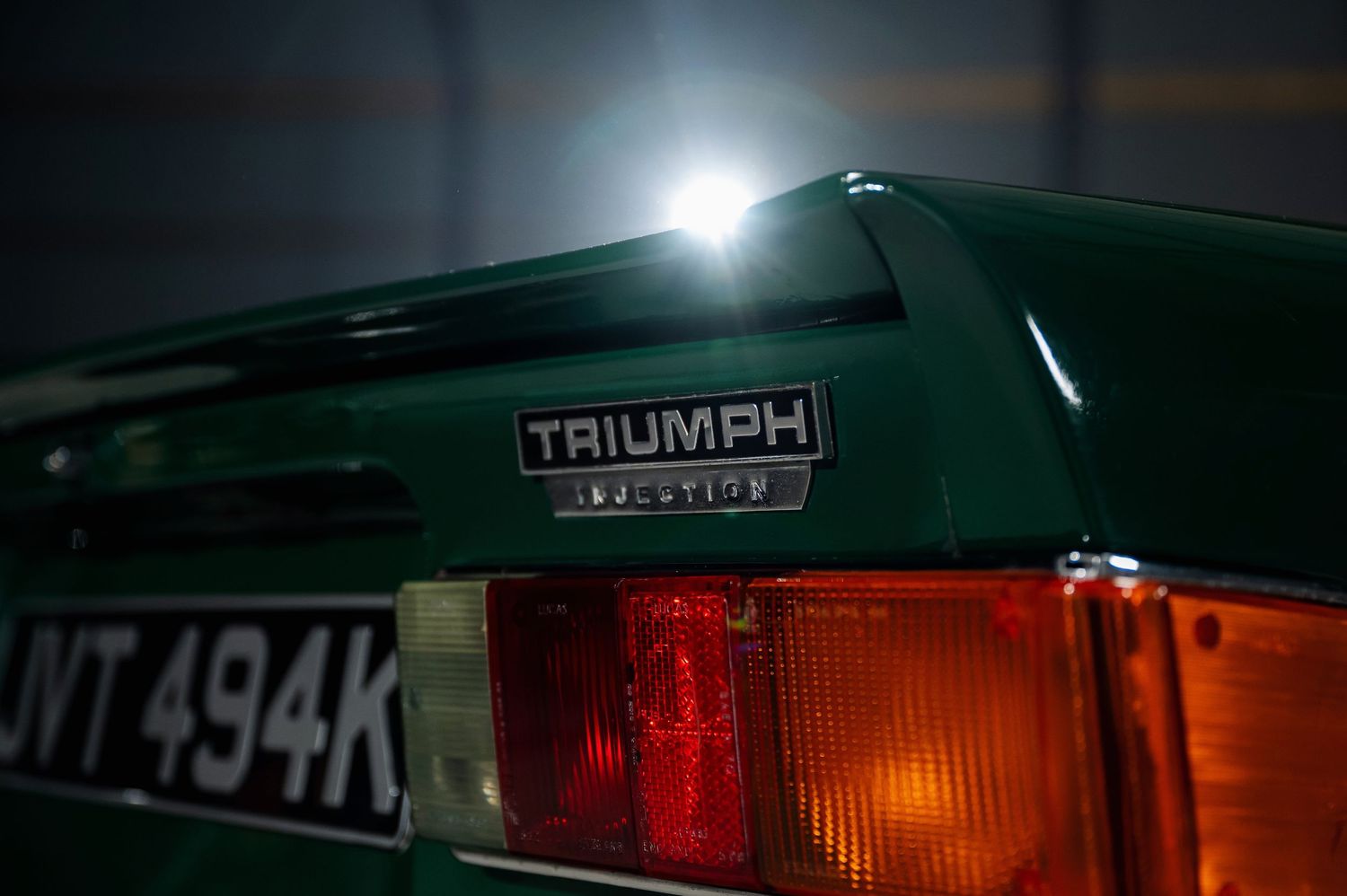 Rear badge detail of a British Racing Green Triumph classic car with red tail lights. Motorist Collection
