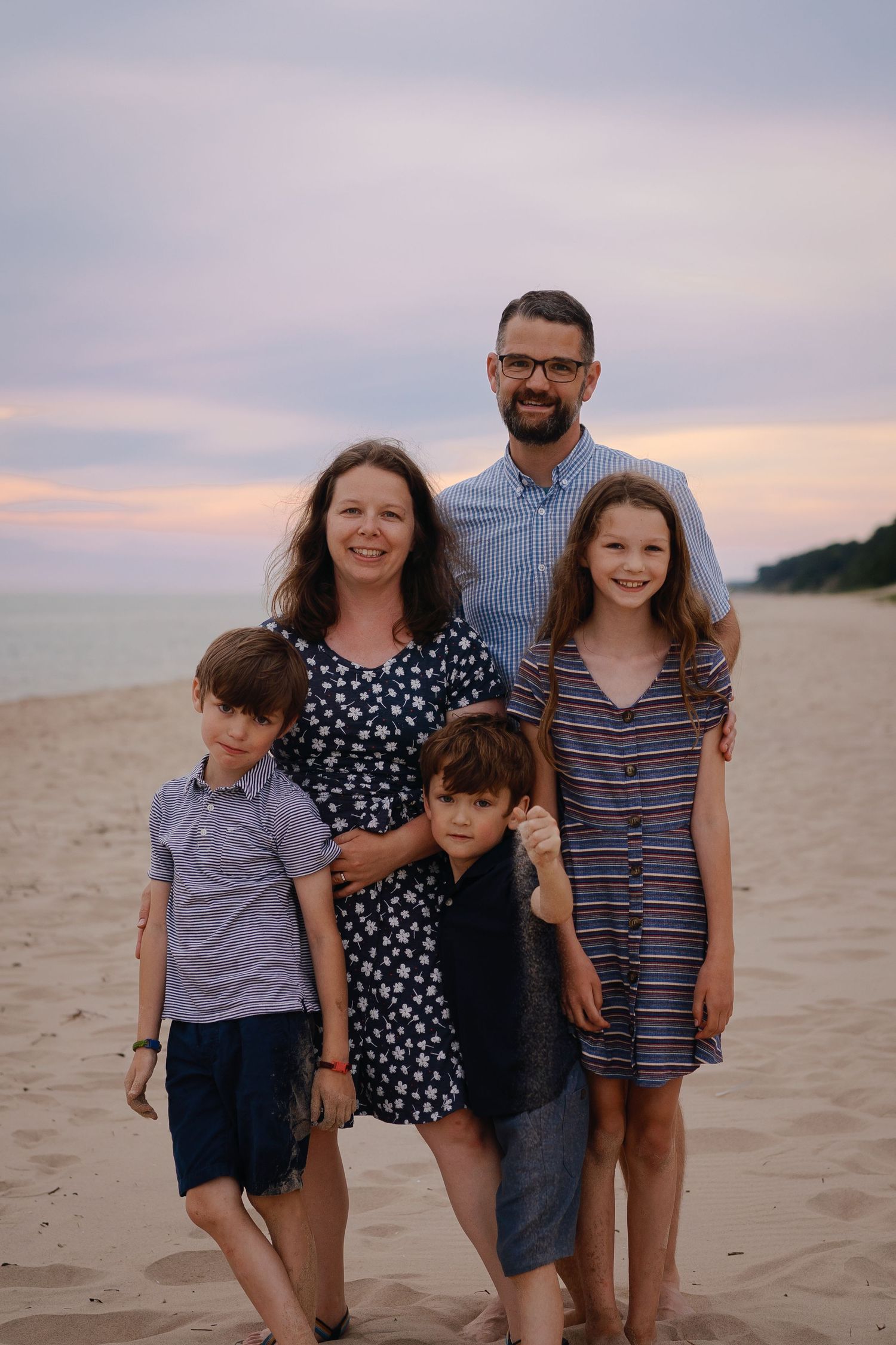 Family poses together for casual portraits on a beach during golden hour.