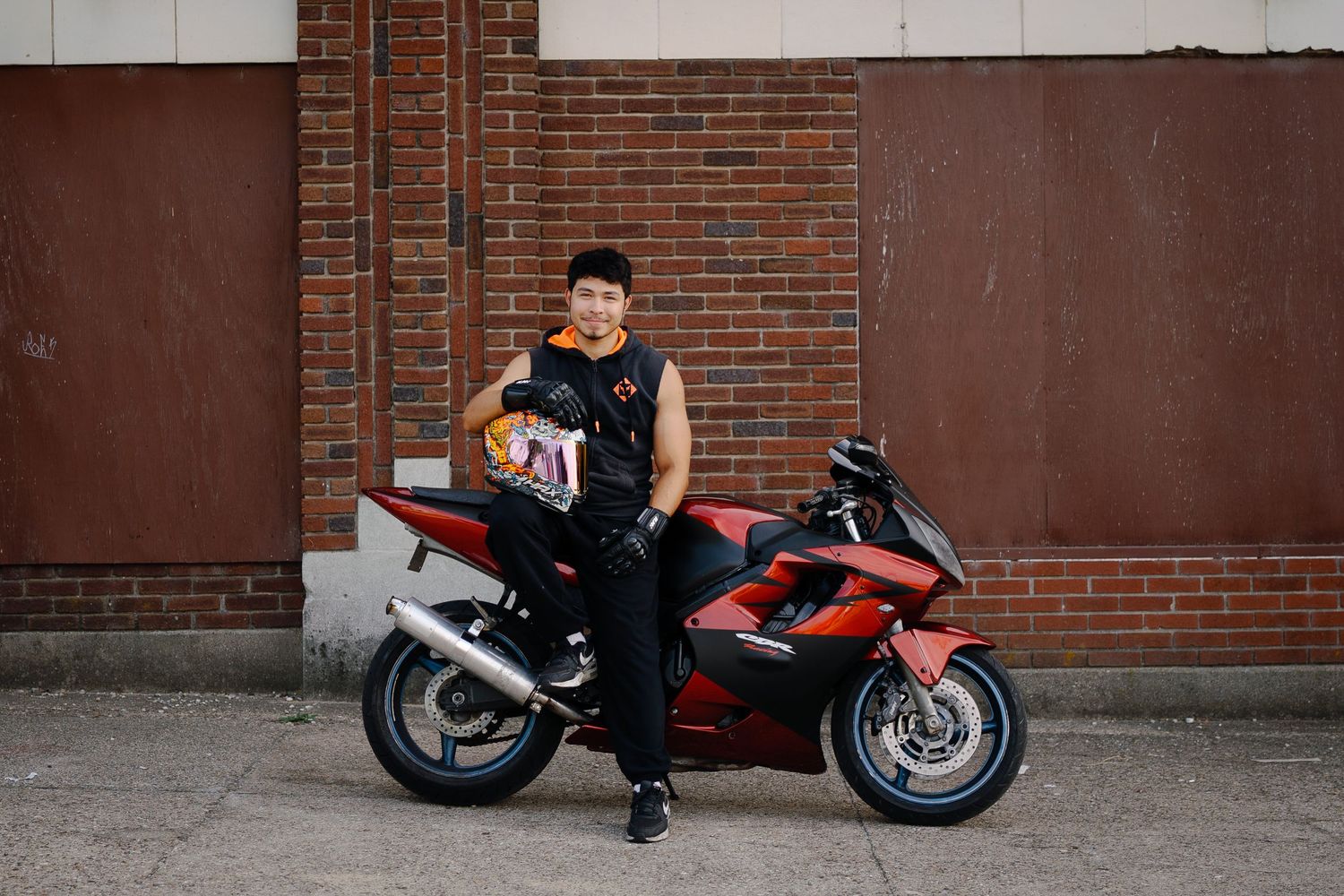 A child poses next to a red motorcycle against a brick wall.