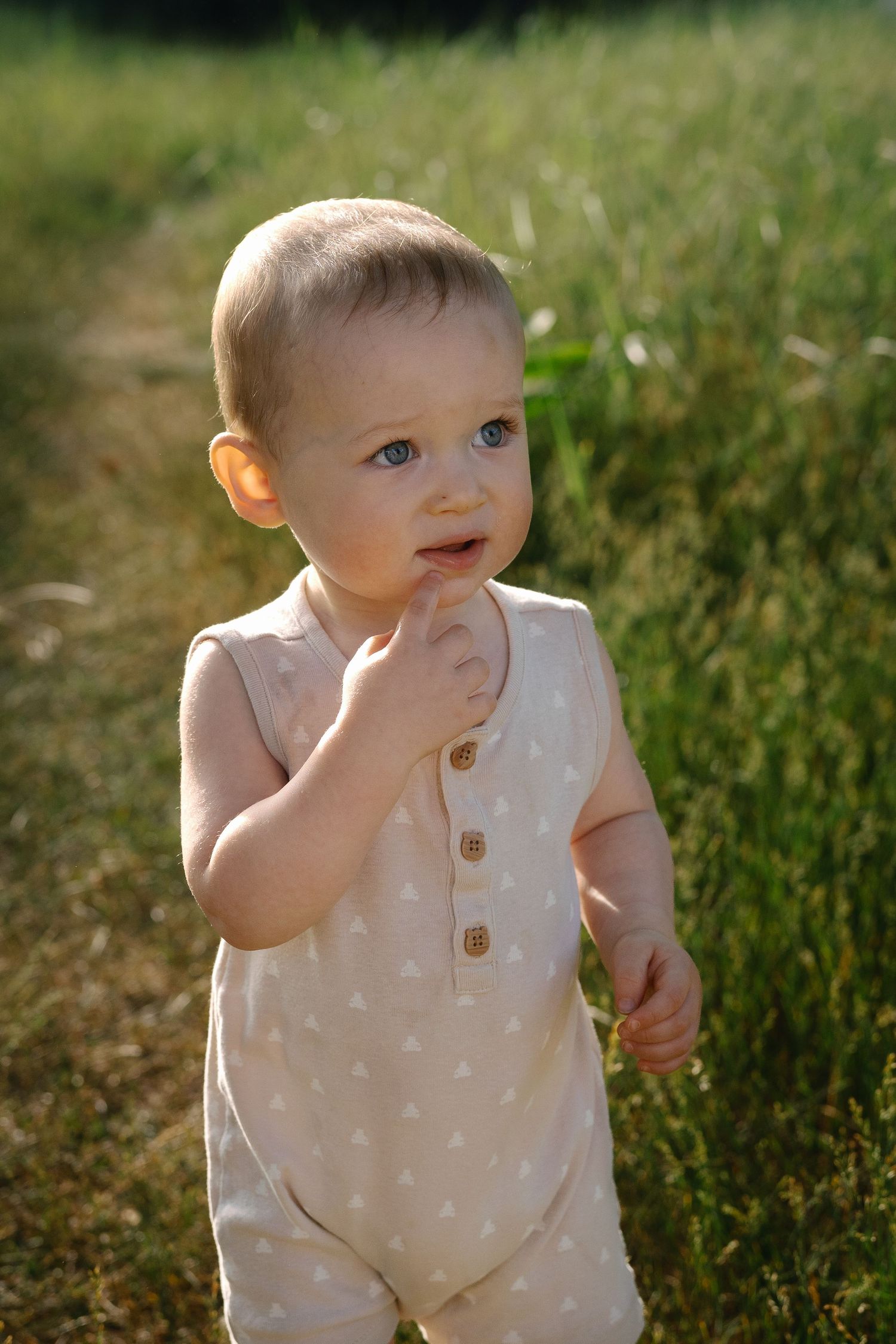 Baby in cream colored romper plays outdoors in golden sunlight.