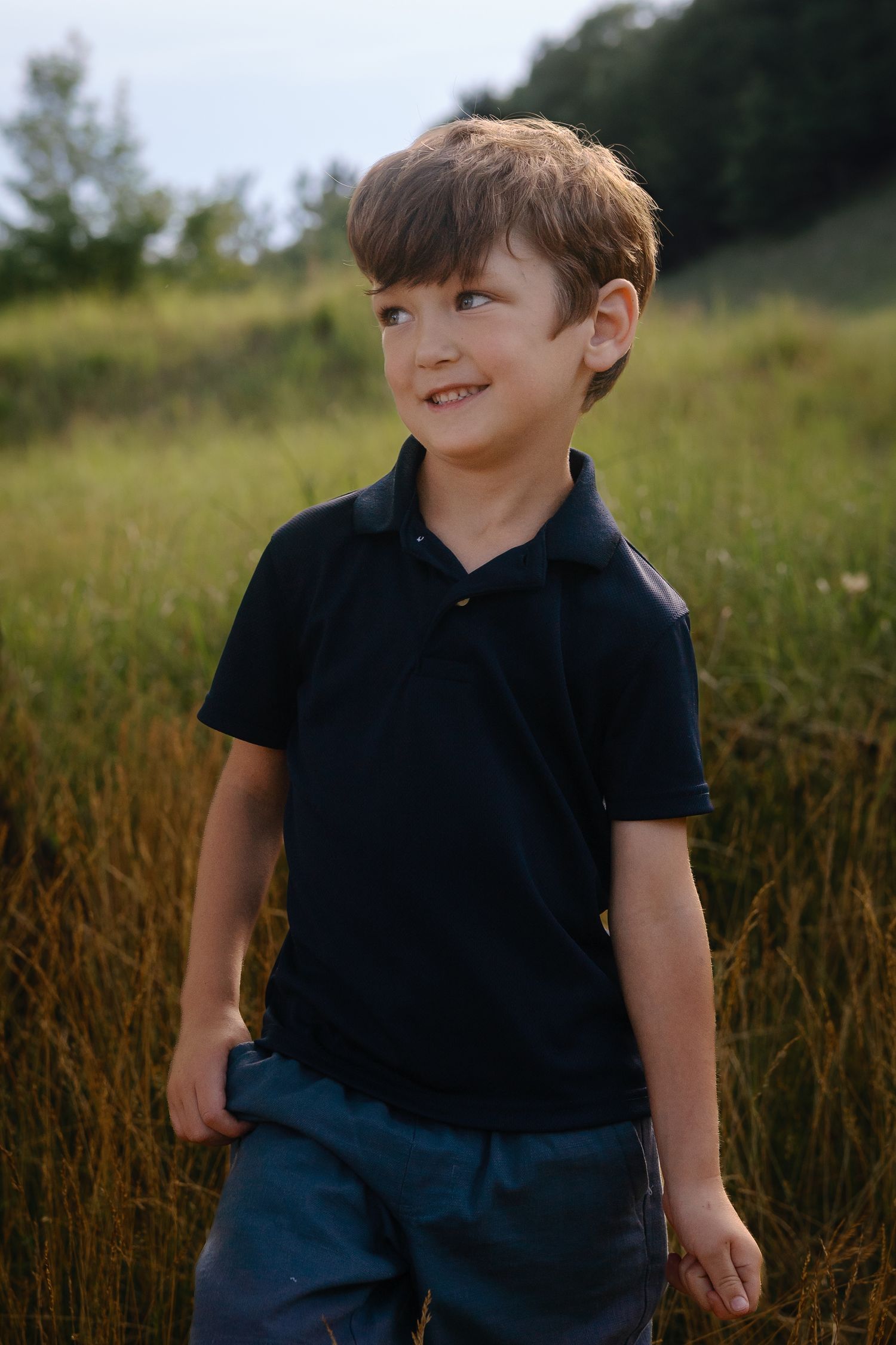 Child in navy blue polo shirt plays in grassy field during golden hour.