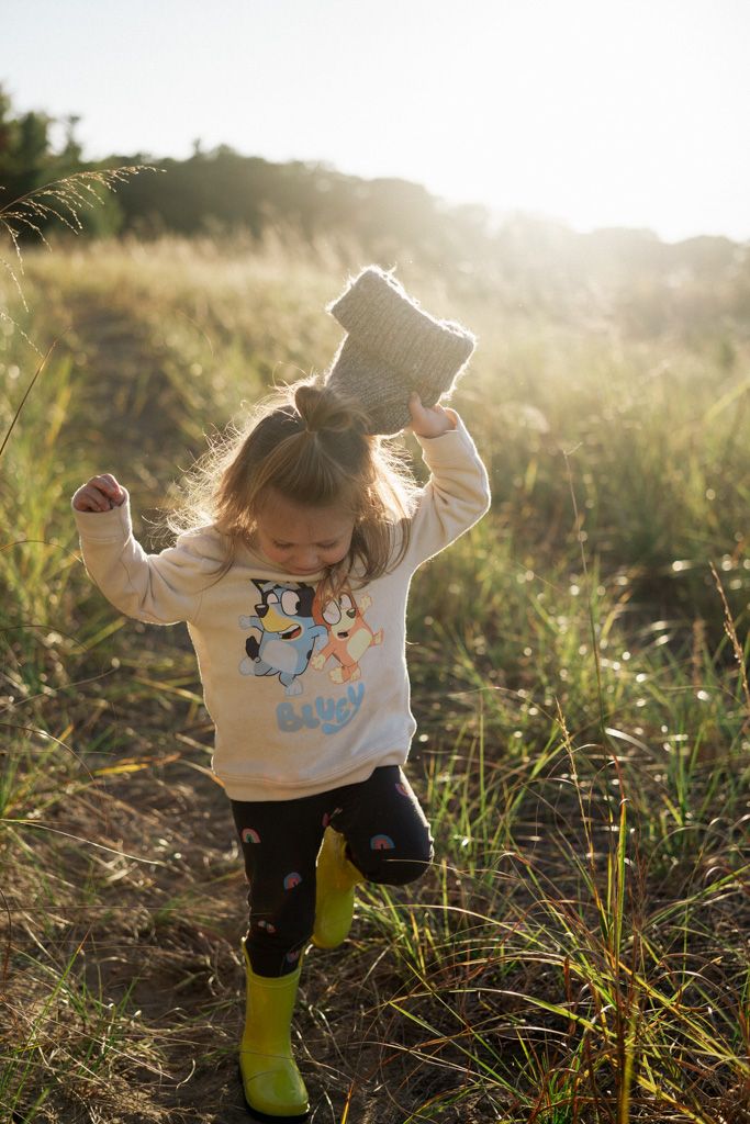 Small child in a cream sweater plays in tall grass during golden hour.