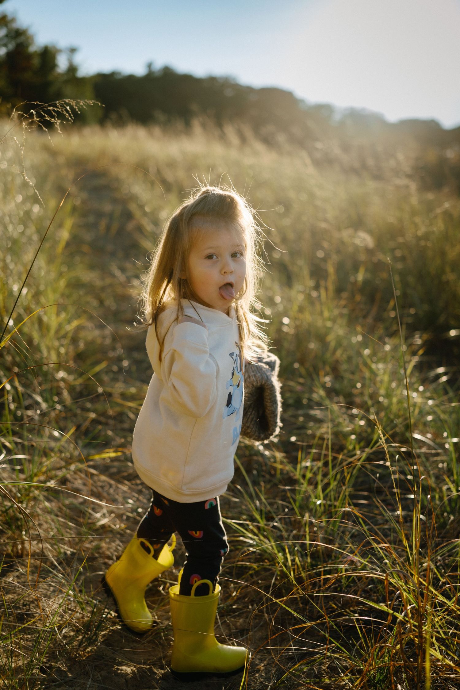A child in yellow boots explores tall grass during golden hour.