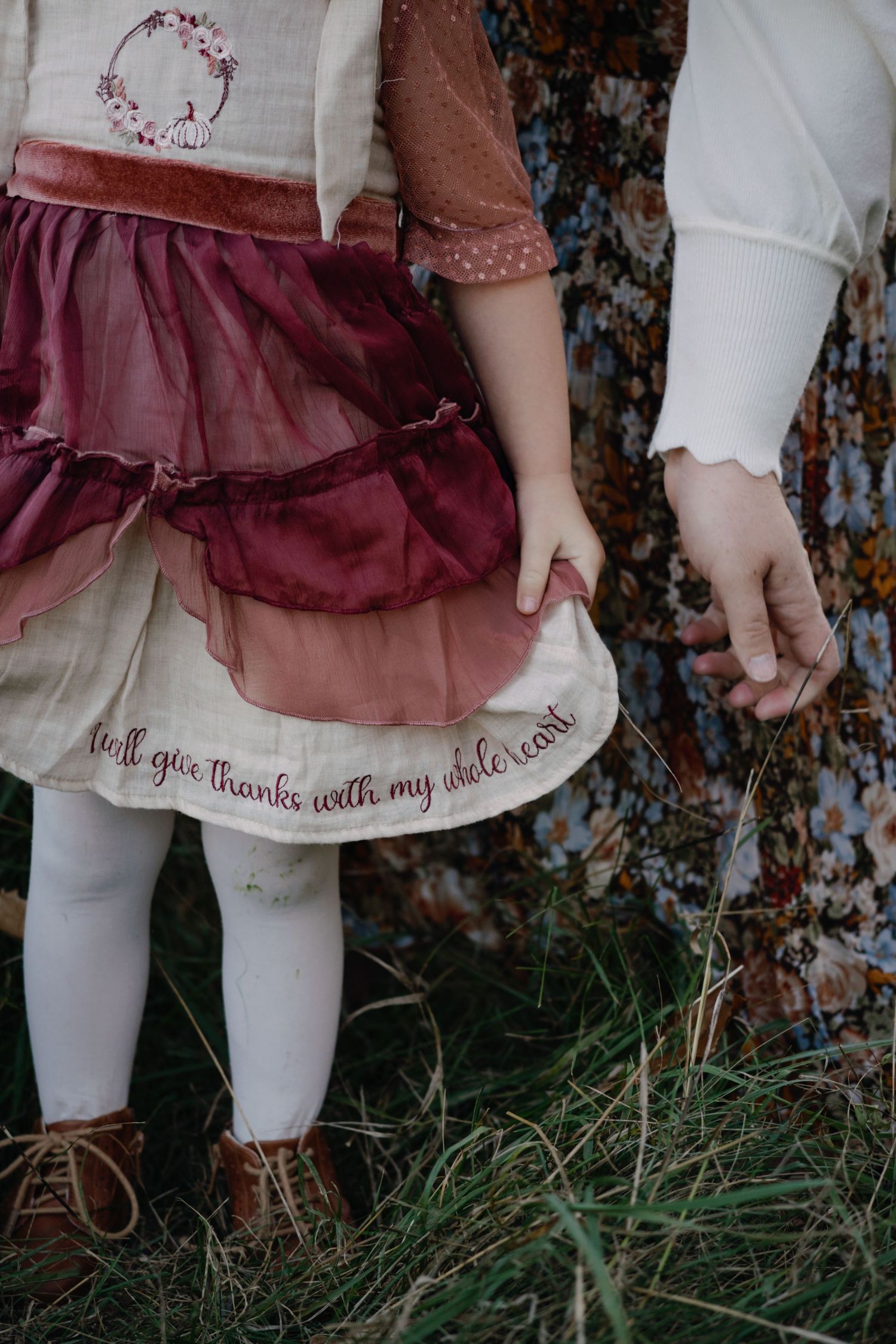 Close-up of embroidered dress details and white tights against natural grass background.