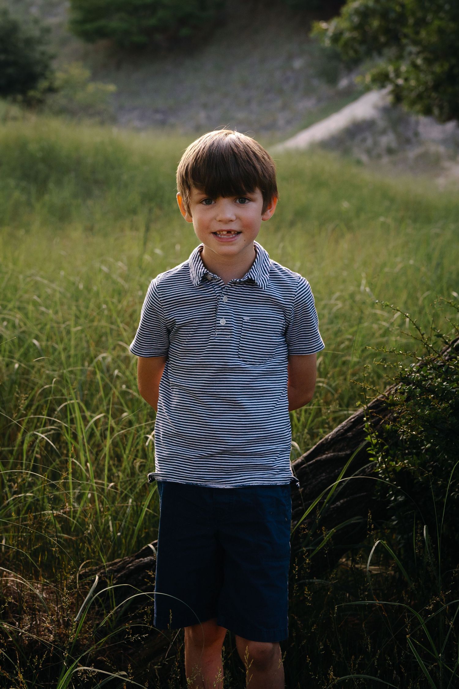 Young child in striped polo shirt smiles while standing in tall grass.