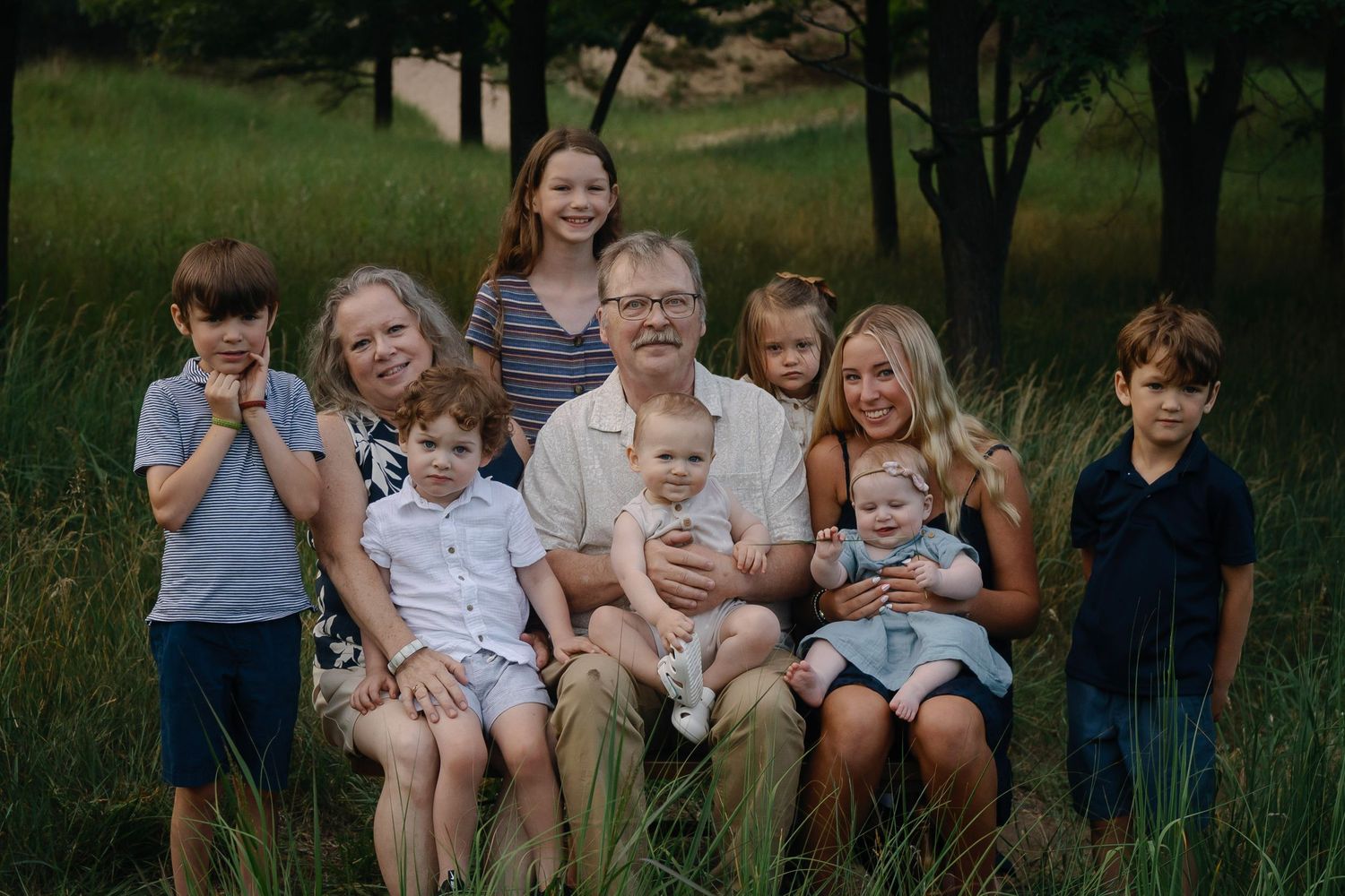 Multi-generational family sits together outdoors on a wooden bench surrounded by nature.
