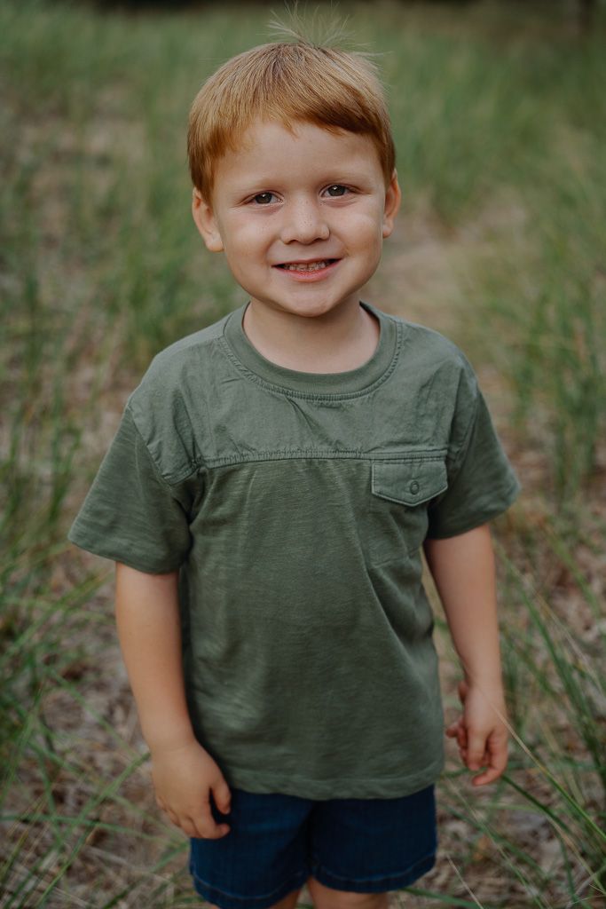 Young child wearing a green t-shirt and denim shorts stands in a grassy outdoor setting.